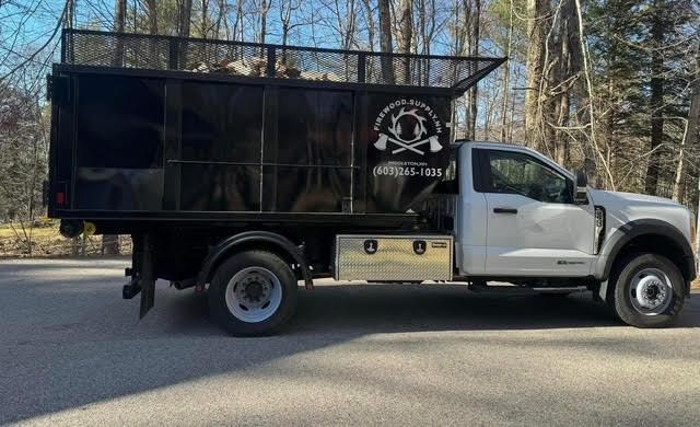 White dump truck with black cargo bed parked on a road in a wooded area