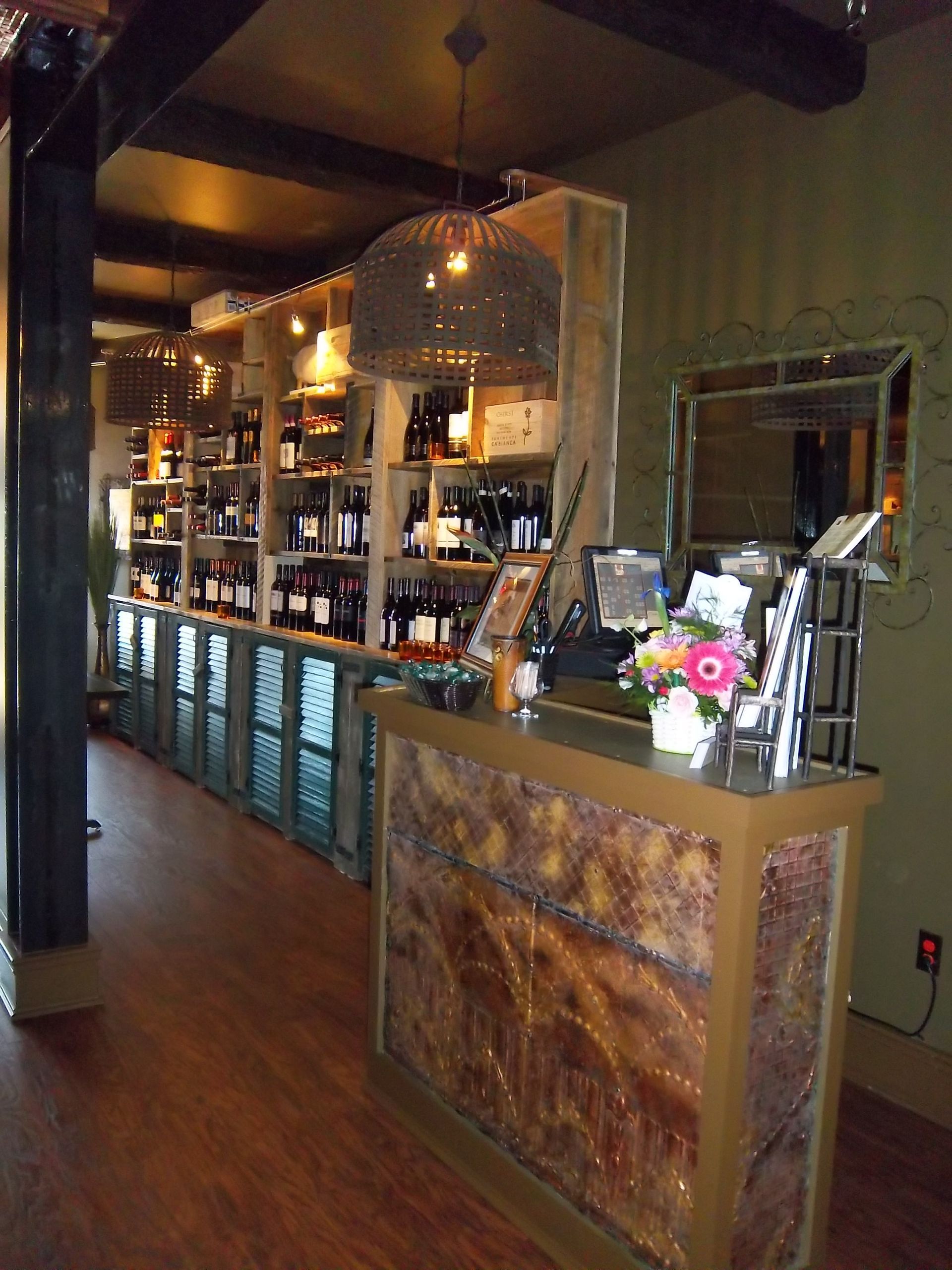 A check-in counter with a textured front in a rustic-style retail space featuring wine shelves and decorative lighting.