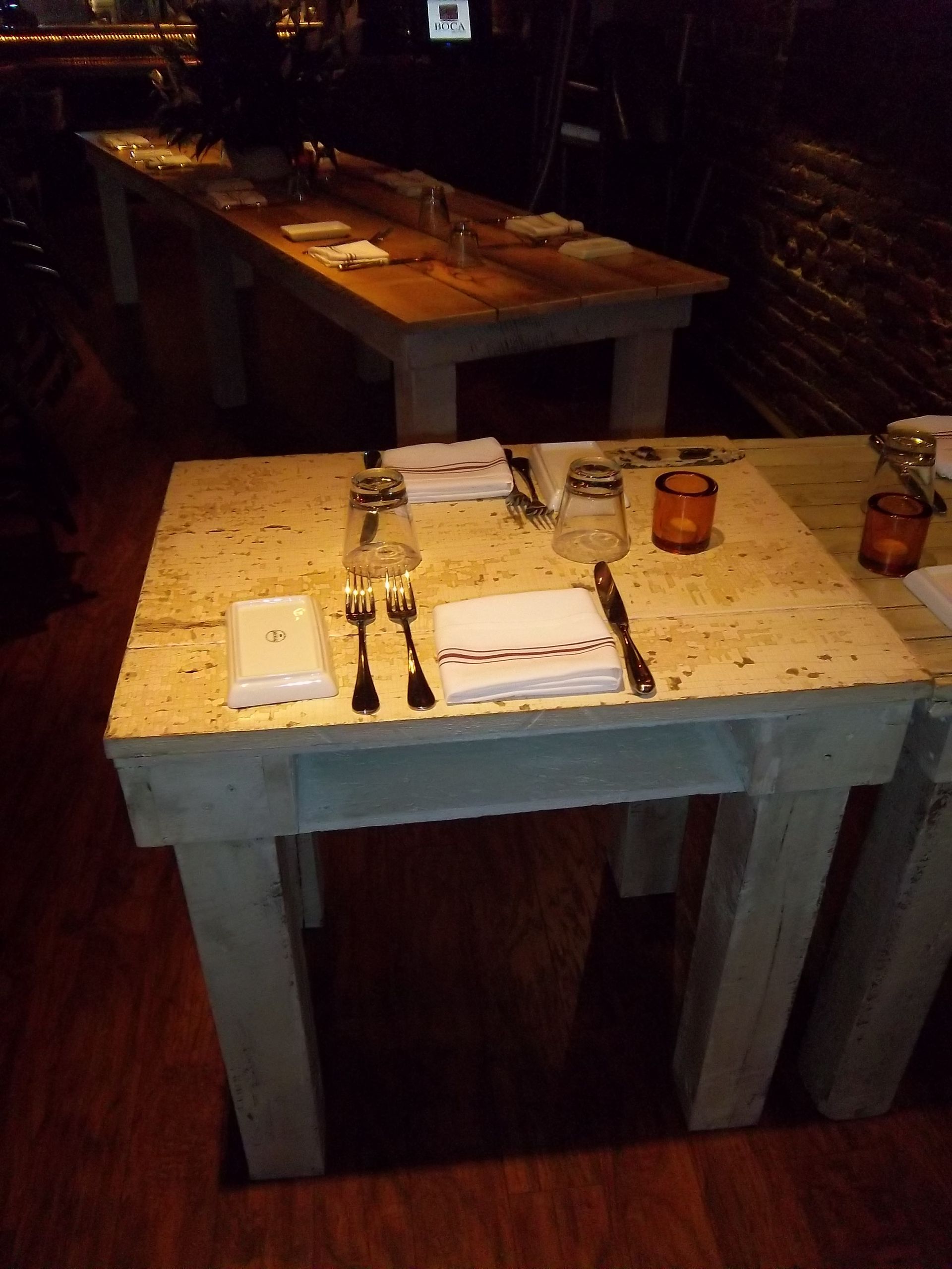 A close-up of a small, square table set for two in a dimly lit, rustic restaurant.