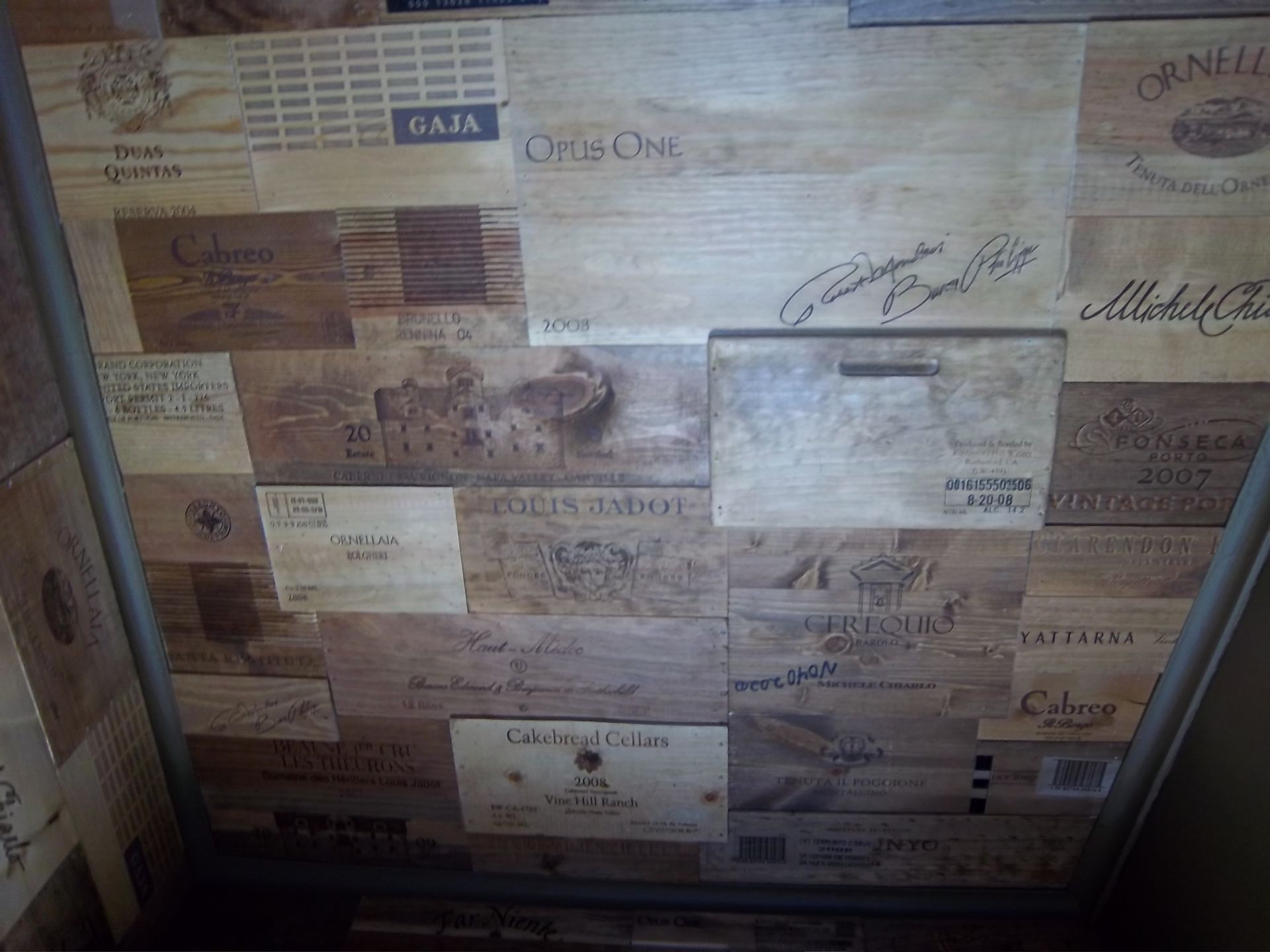 A collage of various branded wooden wine crate panels, arranged to form a textured, light brown rustic wall surface.