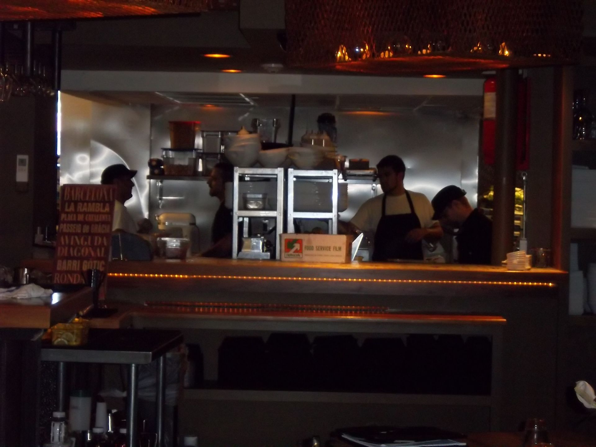 Three kitchen staff members working in an dimly lit restaurant kitchen behind a wooden counter.