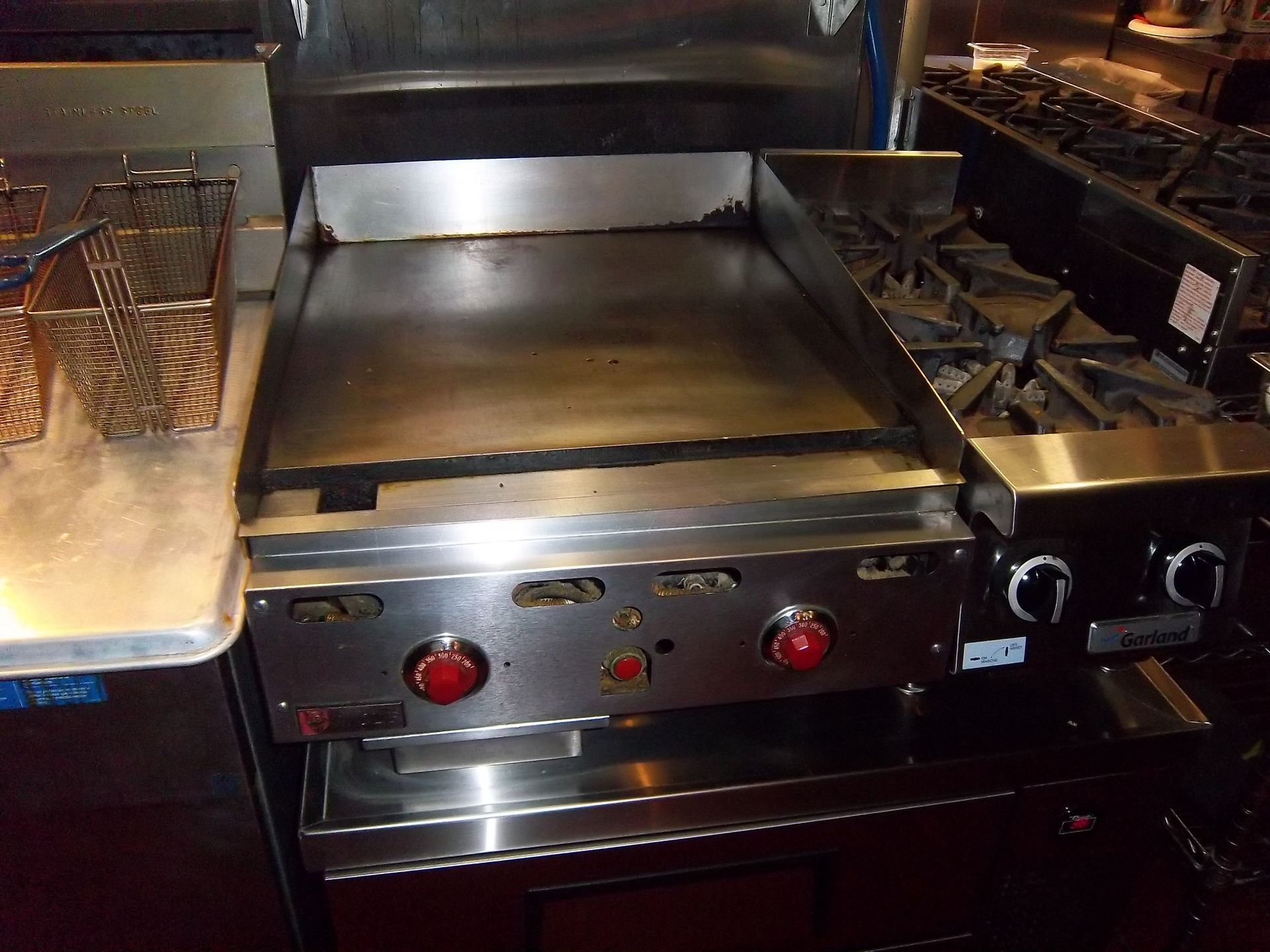A stainless steel commercial kitchen flat-top griddle and a two-burner range sit side-by-side in a kitchen.