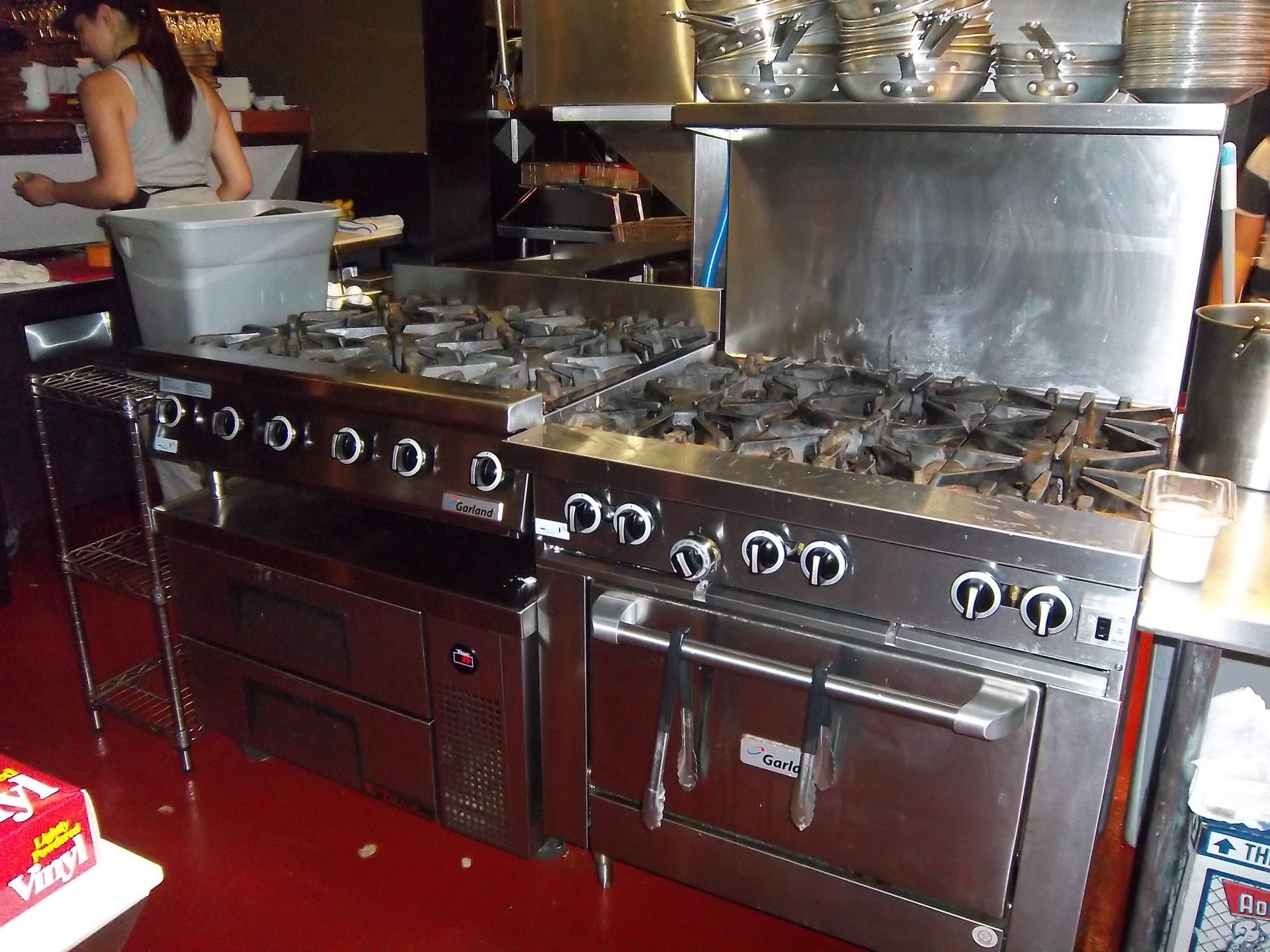 Commercial kitchen with two stainless steel stoves and ovens, with a person standing in the background.