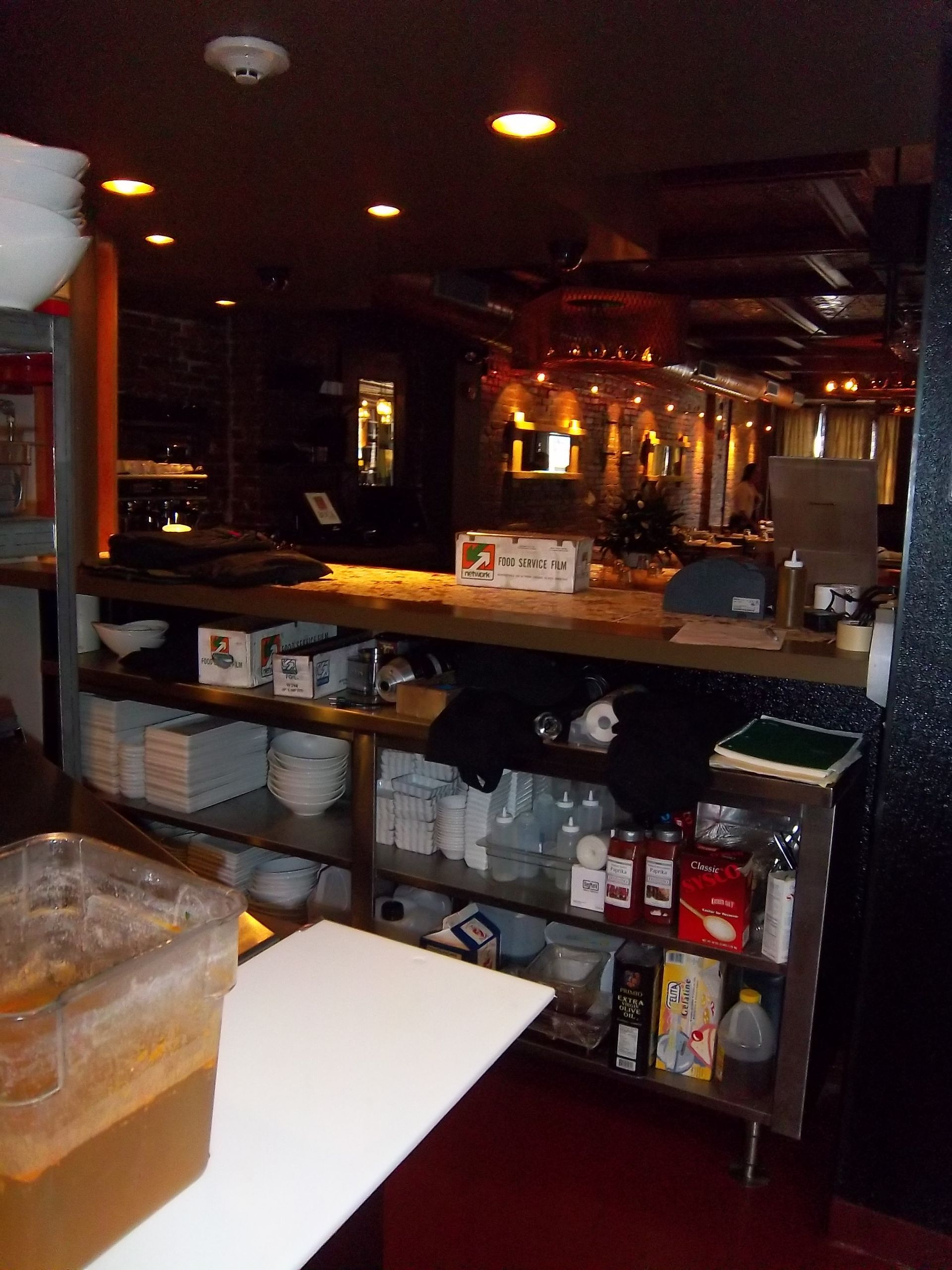 A restaurant serving counter with shelves stocked with white bowls, containers, and supplies in a dimly lit setting.