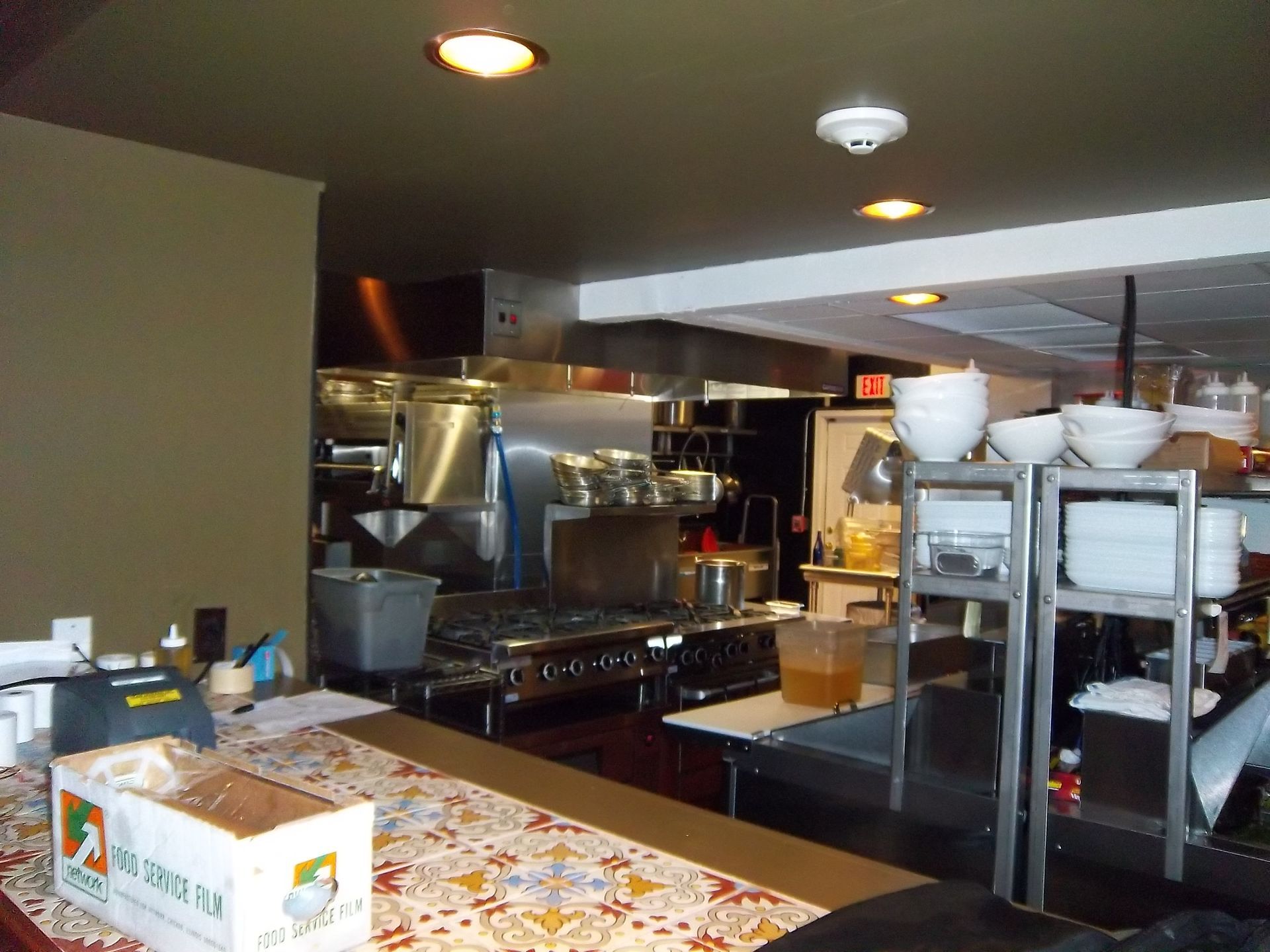 A dimly lit, commercial restaurant kitchen with stainless steel appliances, stacked white bowls, and a service counter.