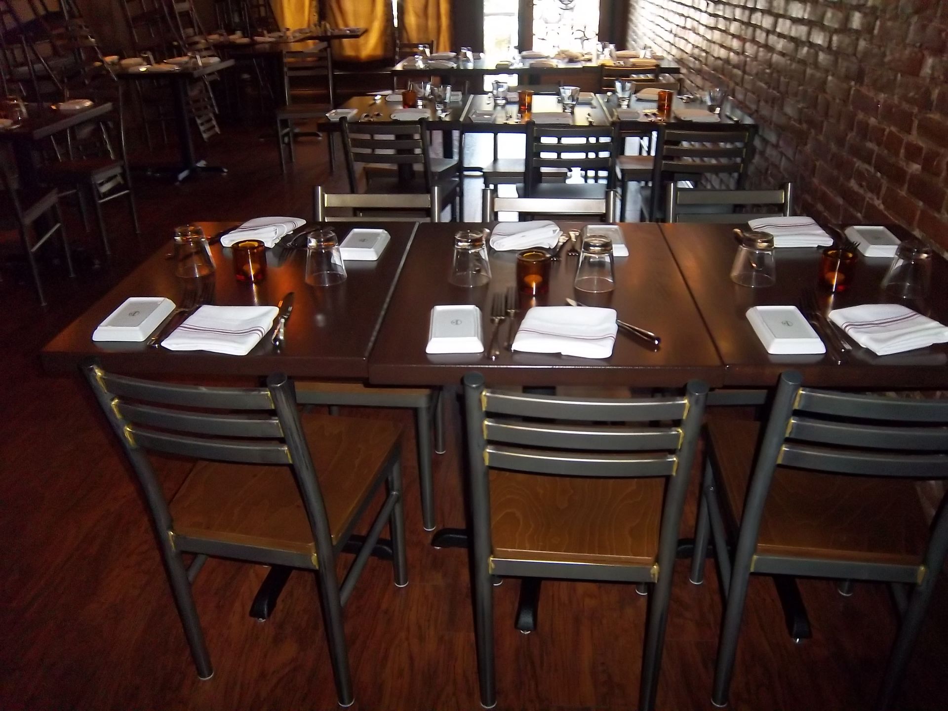Several tables with white napkins and glassware arranged for dining in a restaurant with exposed brick walls.