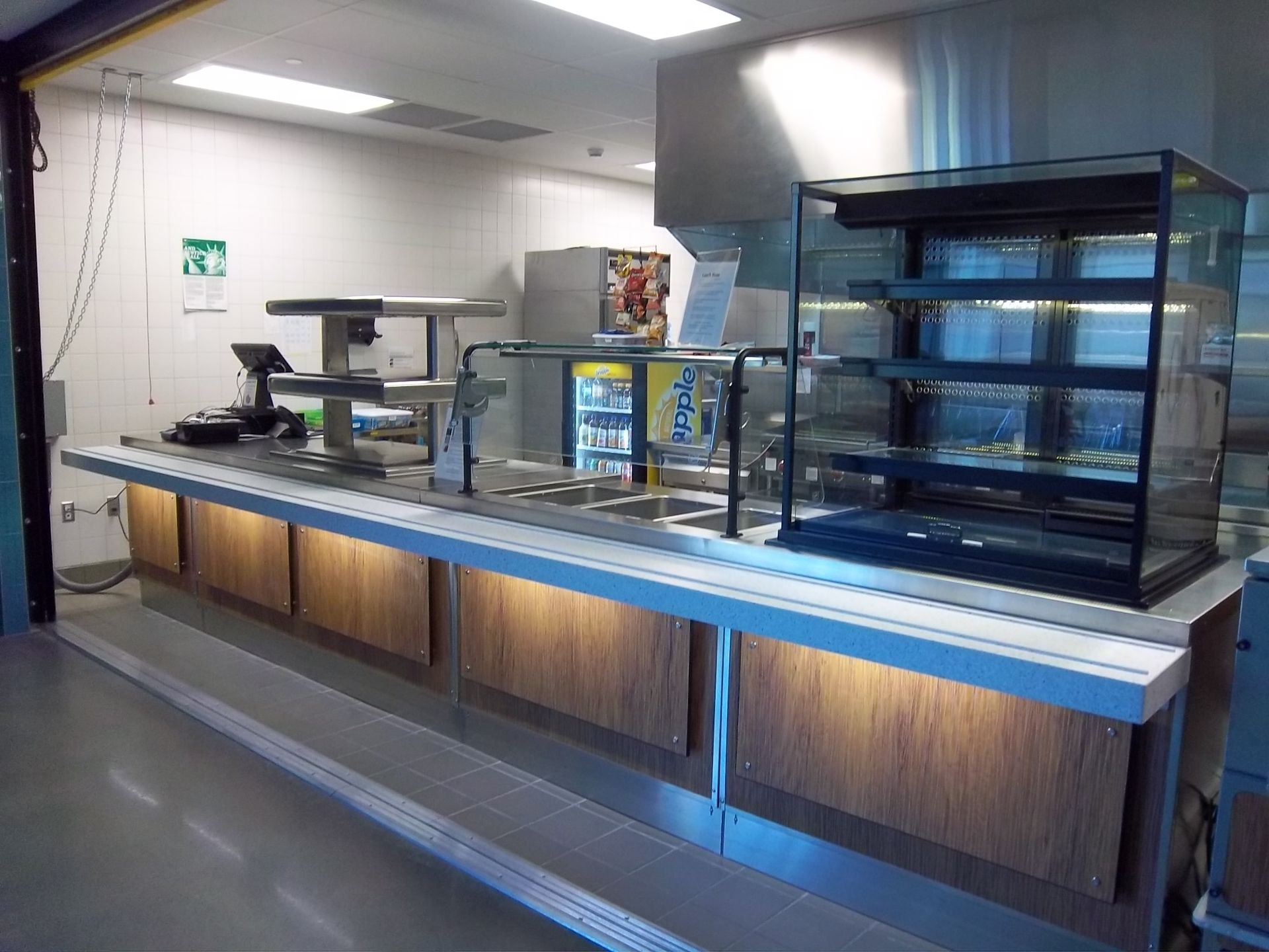 An empty cafeteria service counter with a glass display case, wooden panels, and under-counter lighting.