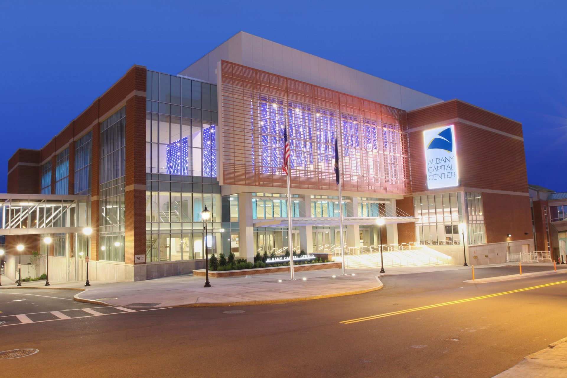 A modern brick and glass building illuminated at night with a decorative metal facade and streetlights in the foreground.