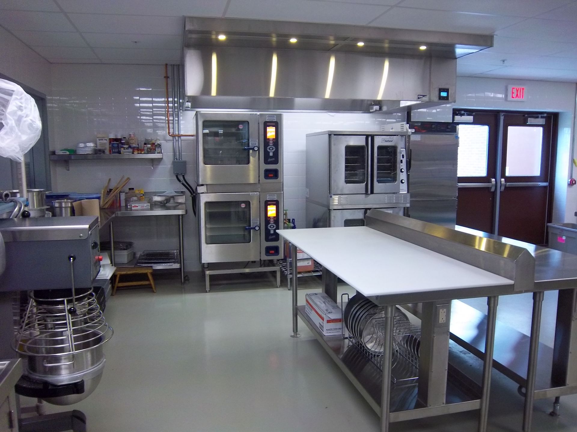 A commercial kitchen with stainless steel appliances, stacked ovens, and food preparation tables.