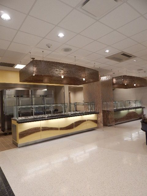 A modern cafeteria serving area with illuminated buffets, sleek counters, and decorative metal light fixtures.
