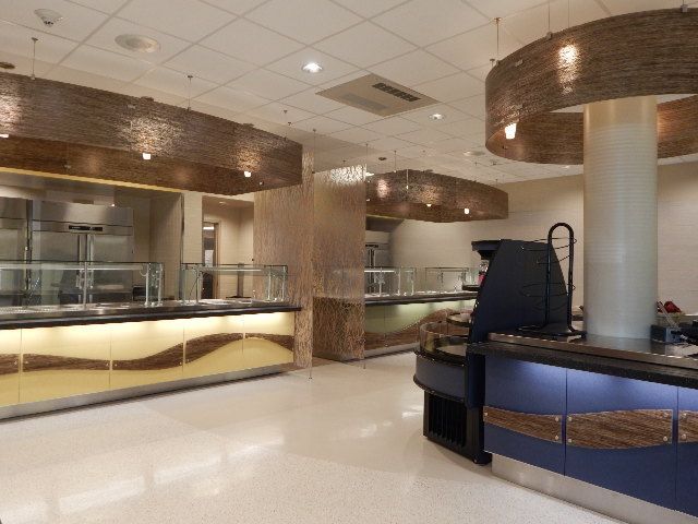 Modern cafeteria serving area with illuminated buffets, textured overhead lighting, and polished floors.