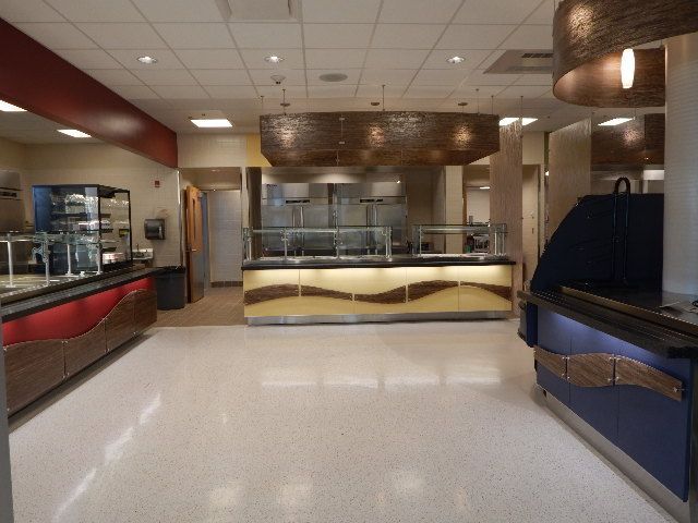 A bright, modern cafeteria serving area with three counter stations featuring red, beige, and blue wave-patterned bases.