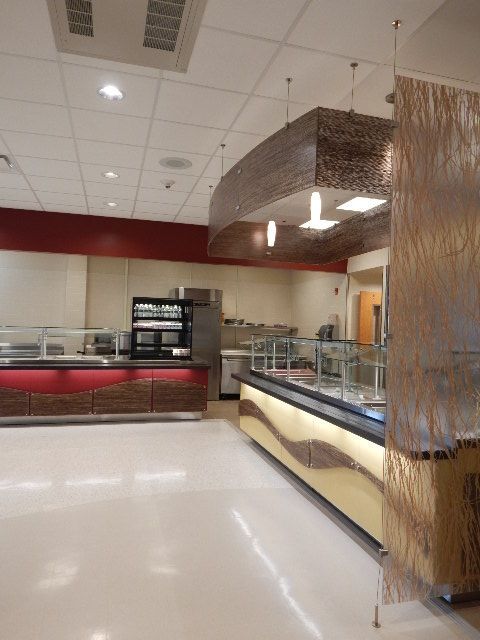 A cafeteria serving area with long buffet counters, warm lighting, and decorative hanging mesh screens.
