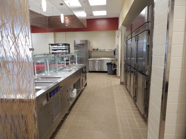 A commercial kitchen with stainless steel counters, food preparation stations, and tall metal refrigerator units.