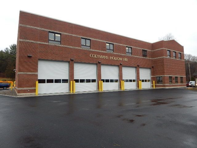 A two-story red brick Columbus Public Works building with five large garage bay doors, viewed from a paved parking lot.