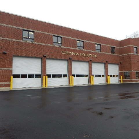 A red brick Coeymans Hollow fire station with five white bay doors and a paved parking lot in front.