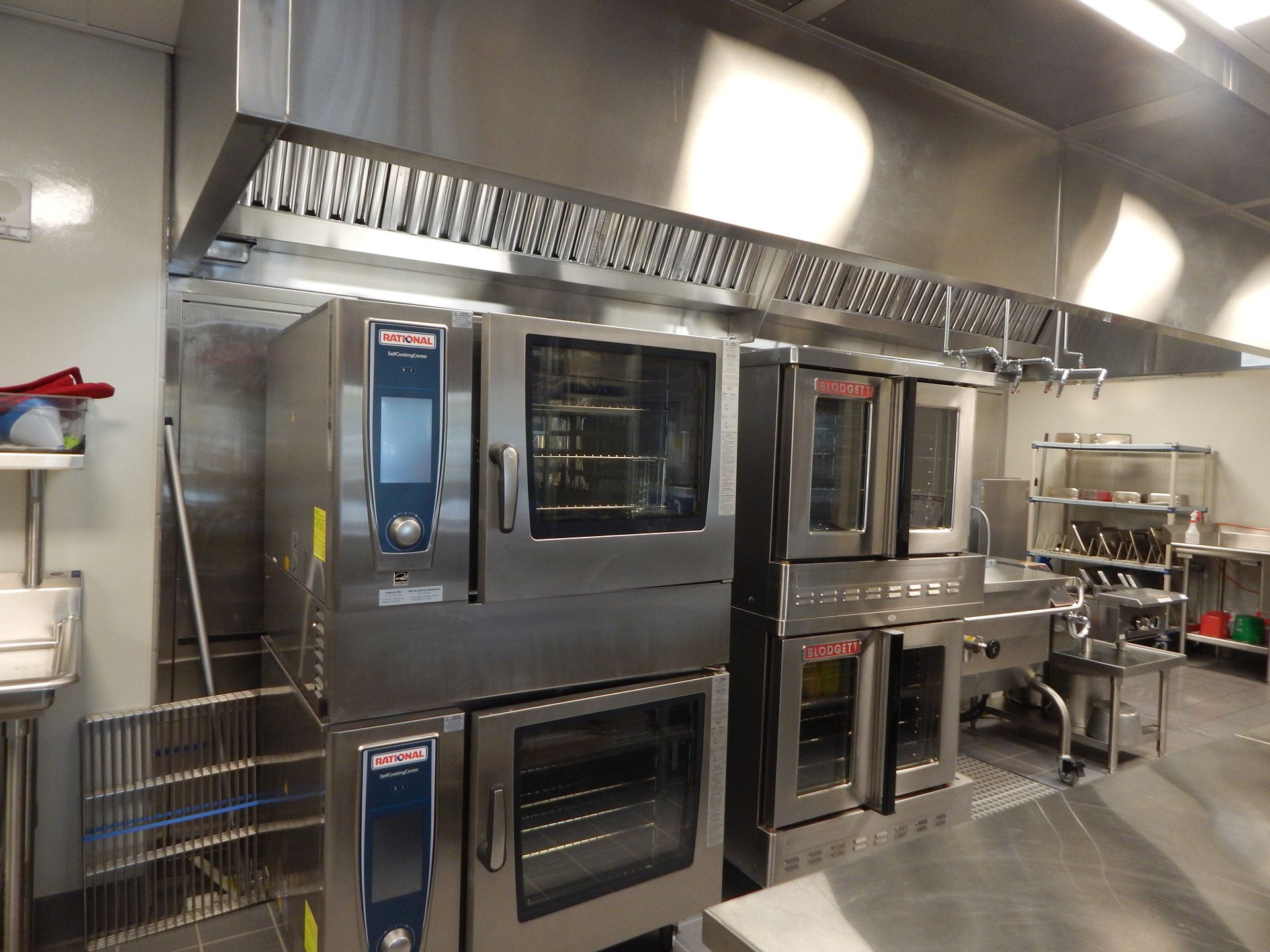 Commercial kitchen featuring stacked stainless steel Rational ovens under a metal ventilation hood.