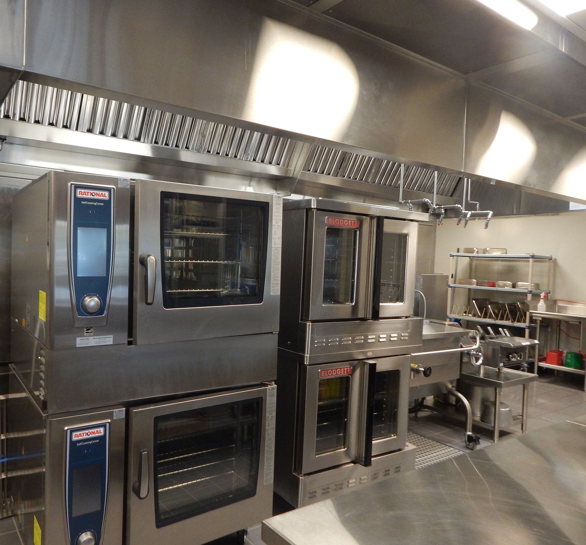 A commercial kitchen featuring stainless steel Rational ovens stacked under a large metal ventilation hood.