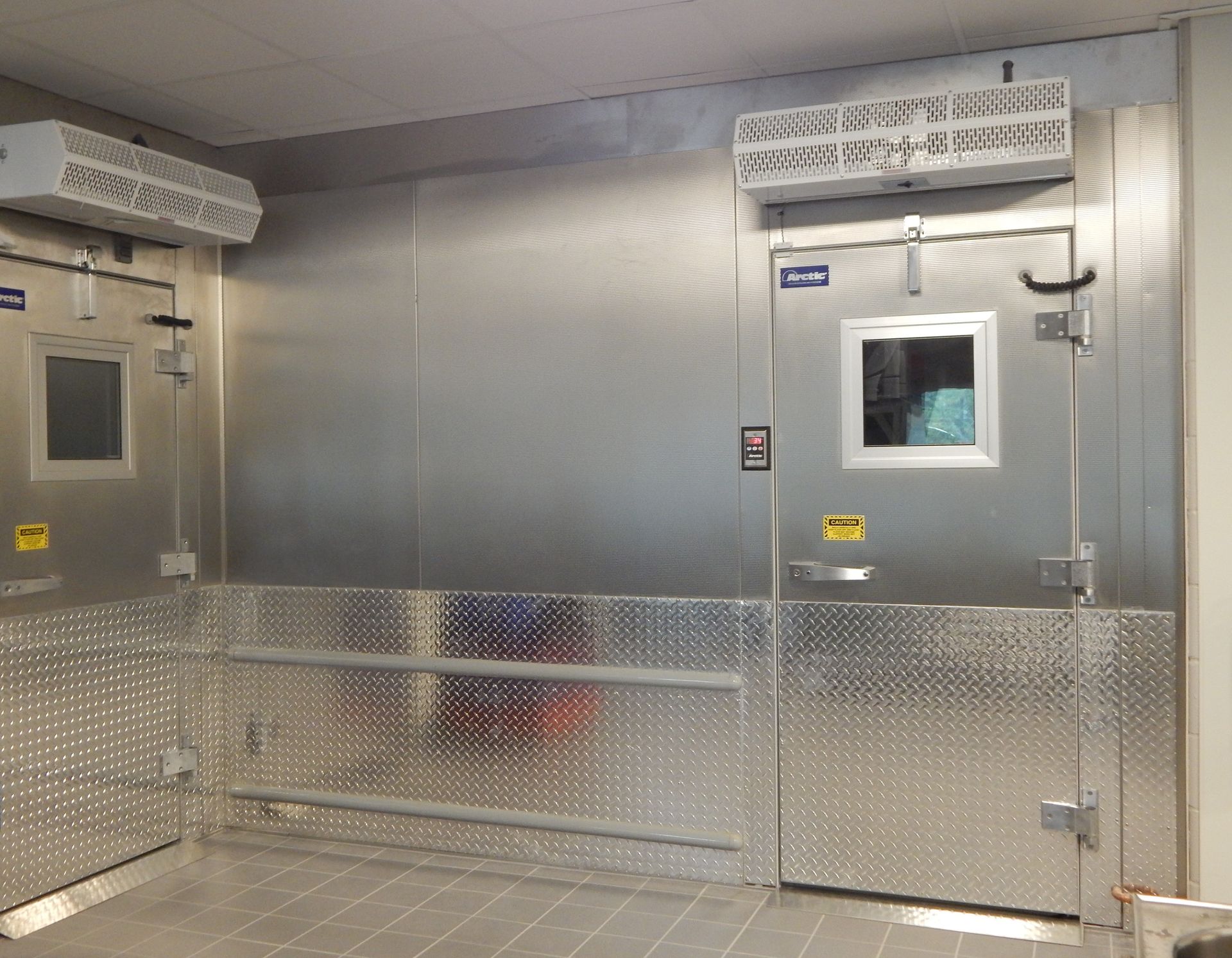 Two industrial walk-in freezer doors made of stainless steel with diamond-plated kickplates and overhead cooling units.