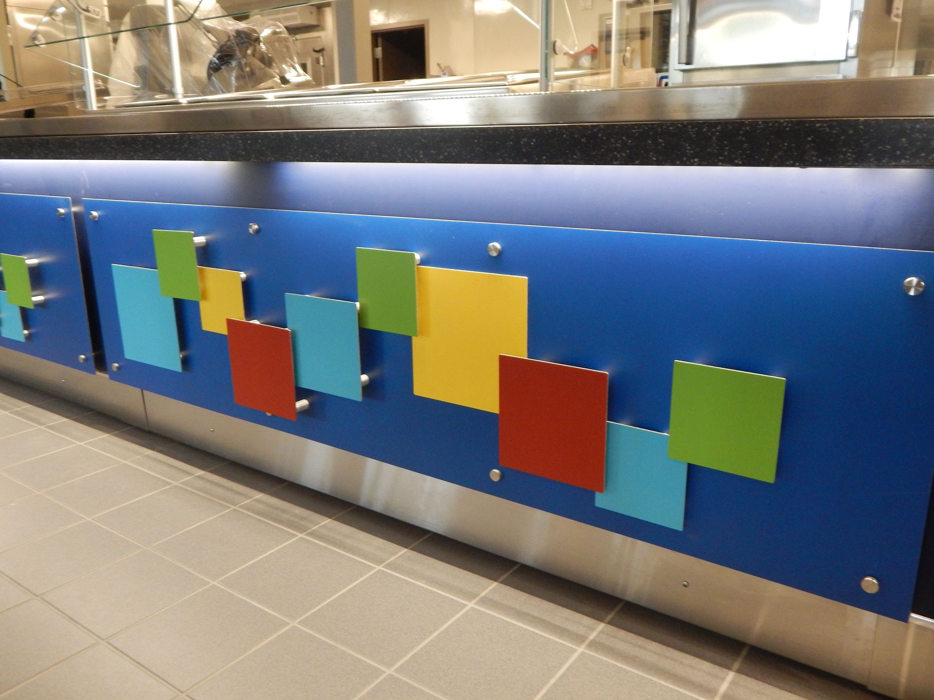 A serving counter with a blue panel decorated with floating, colorful, square-shaped accents in blue, green, and red.