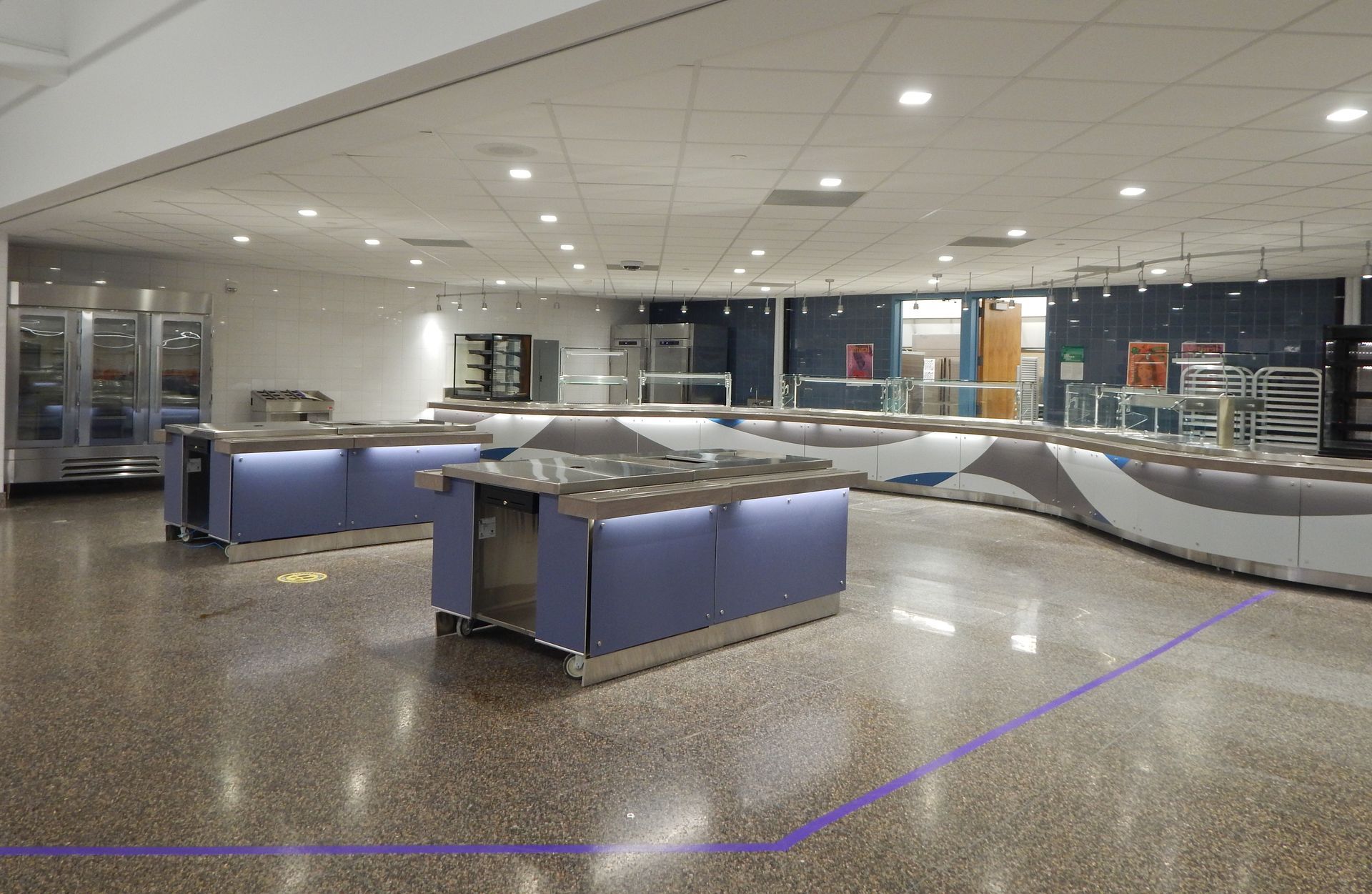 Empty cafeteria service area with blue modular food counters and shiny terrazzo flooring.