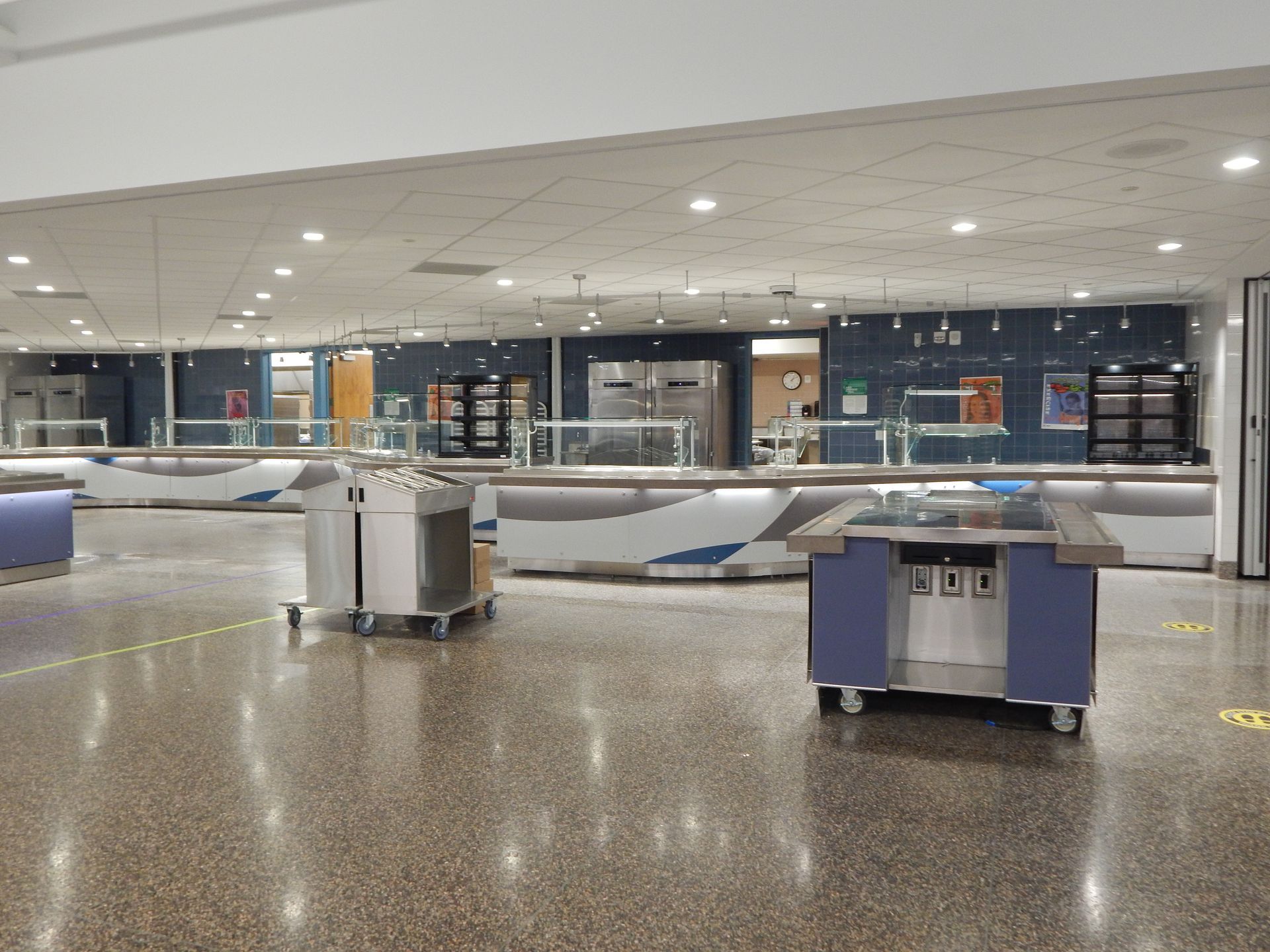 A cafeteria serving area with empty, long counters and a blue and white color scheme on a polished floor.