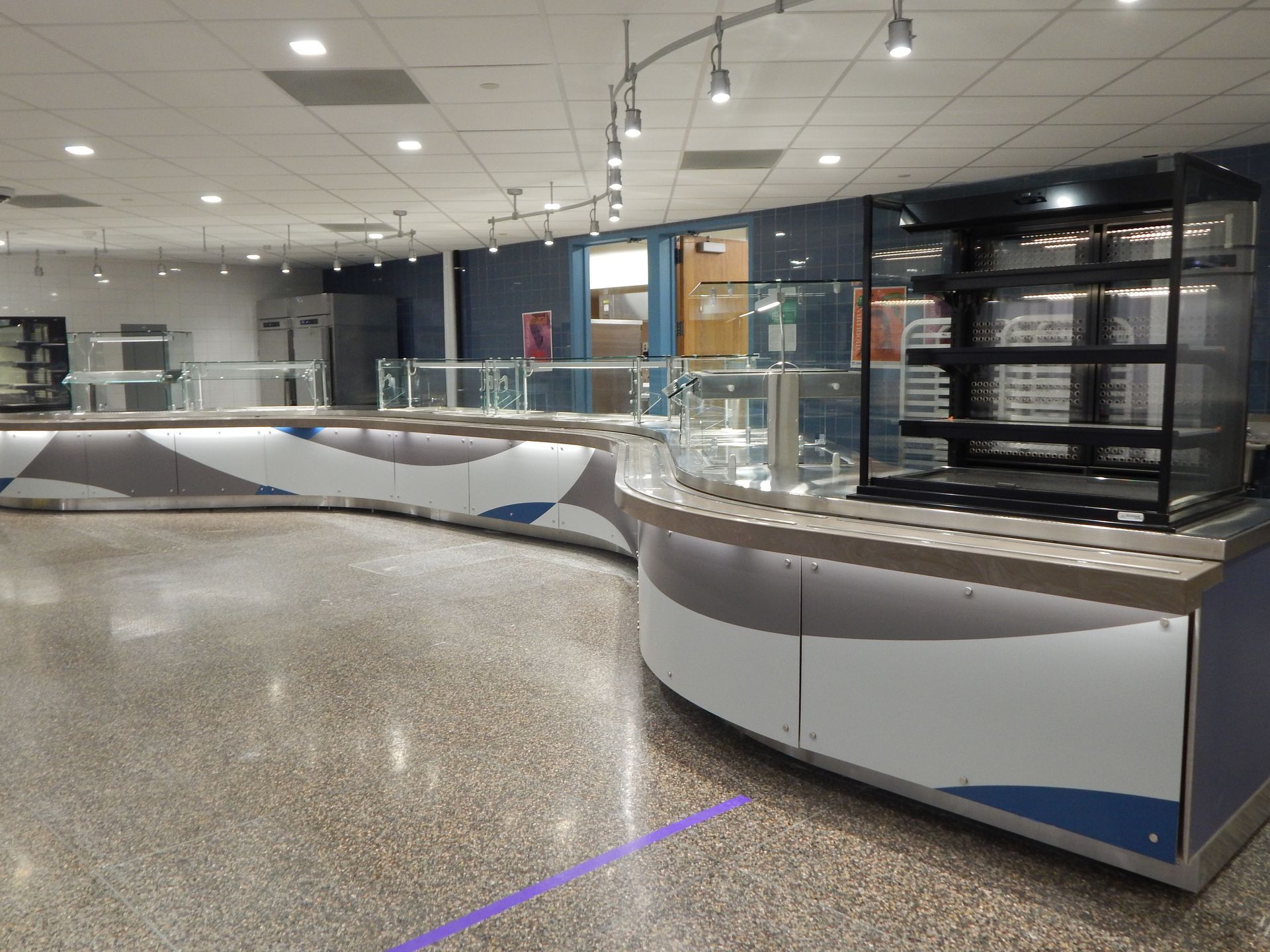 A modern, empty food service counter with glass display shelves and curved, blue and white patterned panels.
