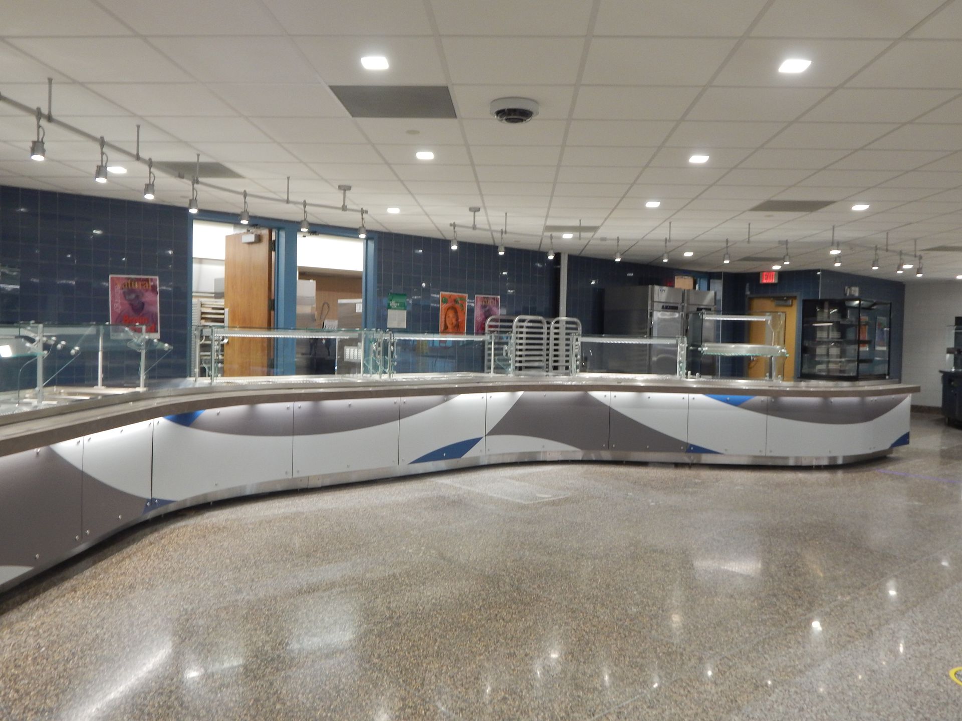 A curved, modern food service counter with blue and white patterned panels inside a tiled, brightly lit dining hall.