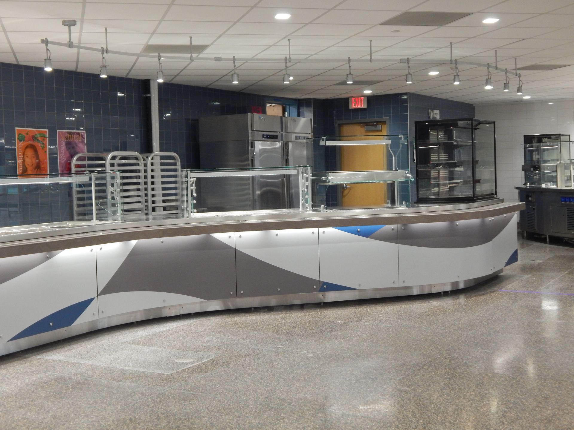 A modern cafeteria serving counter with a curved base in blue, white, and gray, featuring metal racks and equipment.