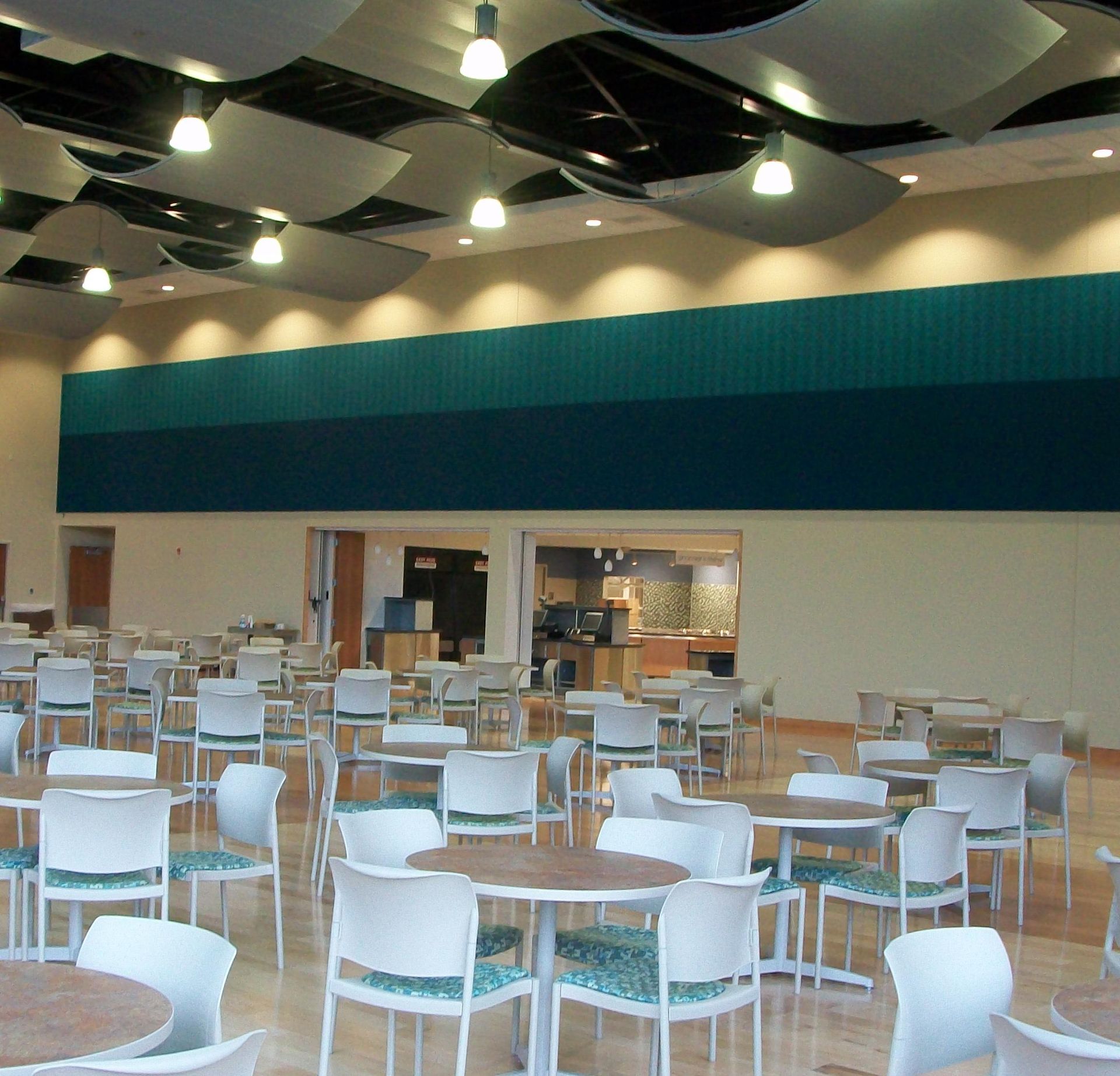 A dining area with round tables and chairs, under a ceiling with acoustic panels and pendant lights.