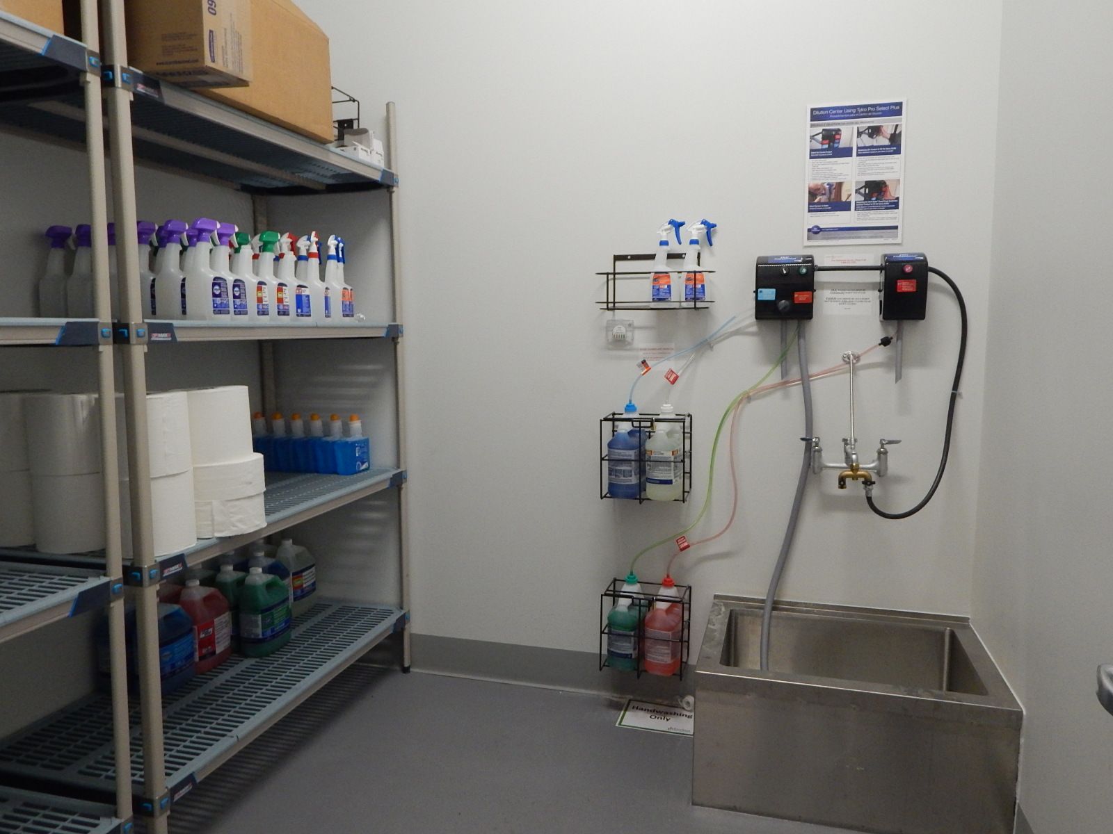 Cleaning supply closet with metal shelving, organized bottles, chemical dispensers on the wall, and a utility sink.