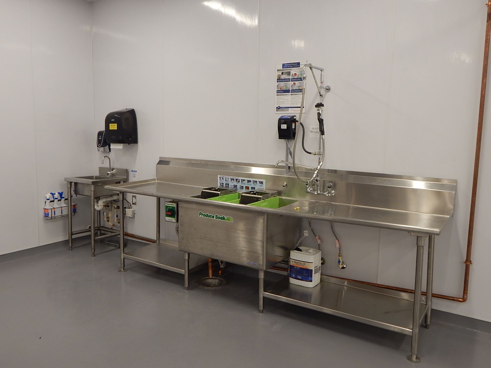 A stainless steel three-compartment sink and a separate handwashing station in a white, commercial kitchen setting.