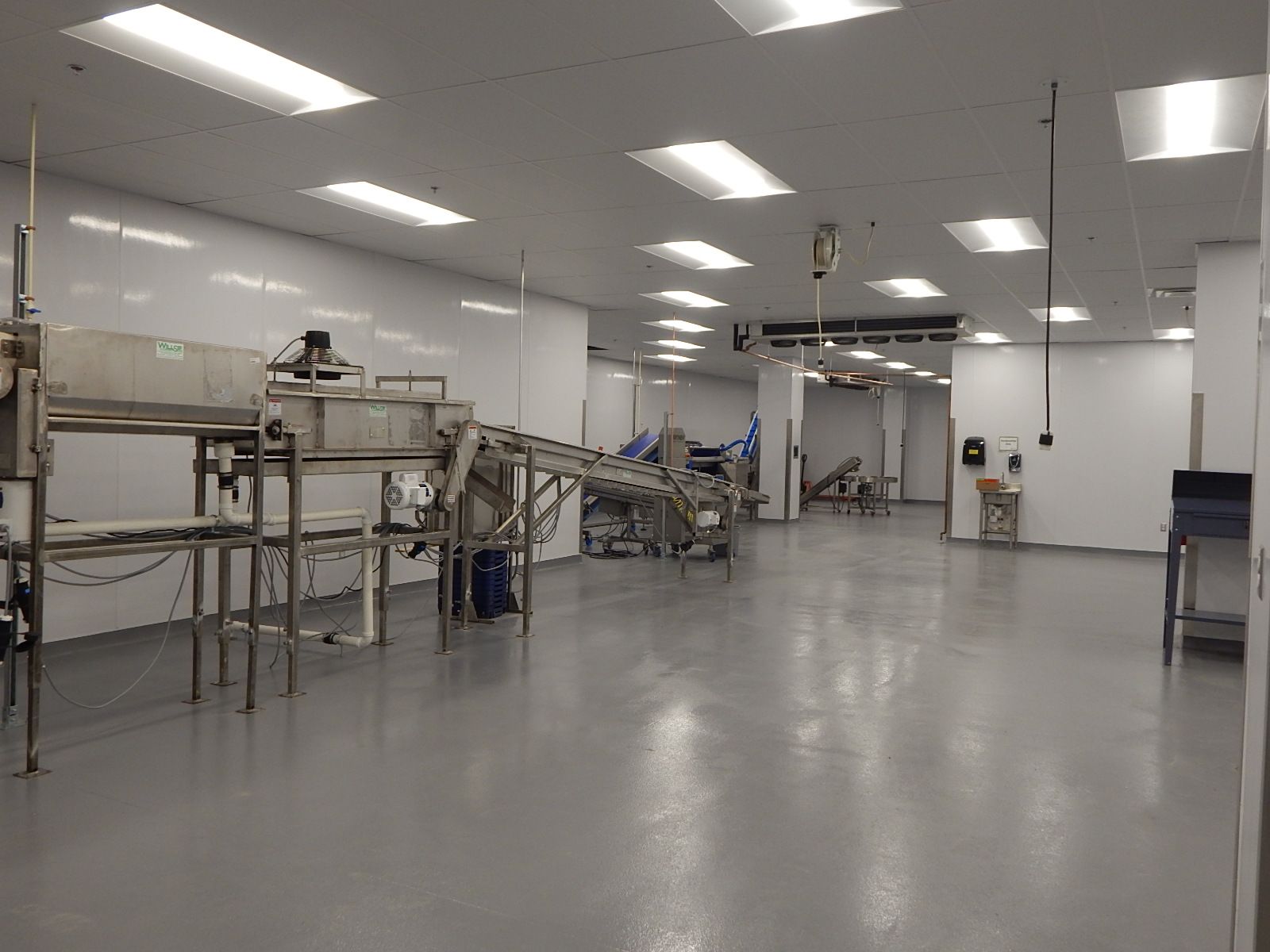 A sterile white food processing room with stainless steel machinery and conveyor belts on a grey floor under ceiling lights.