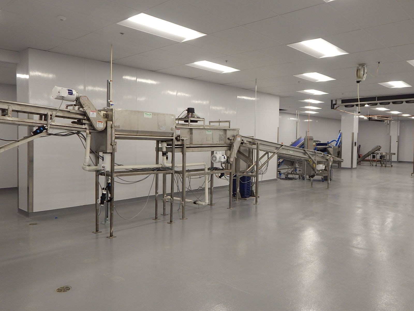 Stainless steel industrial food processing machinery in a clean, brightly lit, white-walled room.