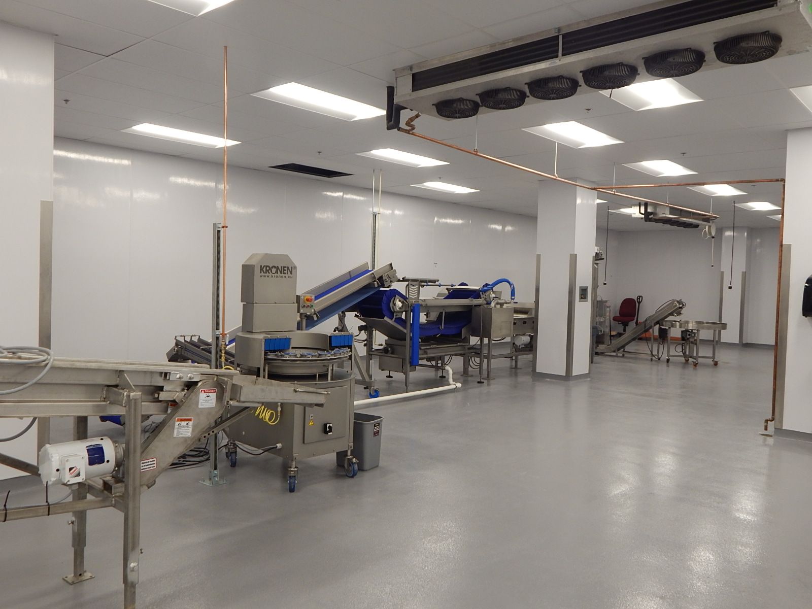 A clean industrial food processing facility with metal machinery, conveyor belts, and white walls under bright ceiling lights.