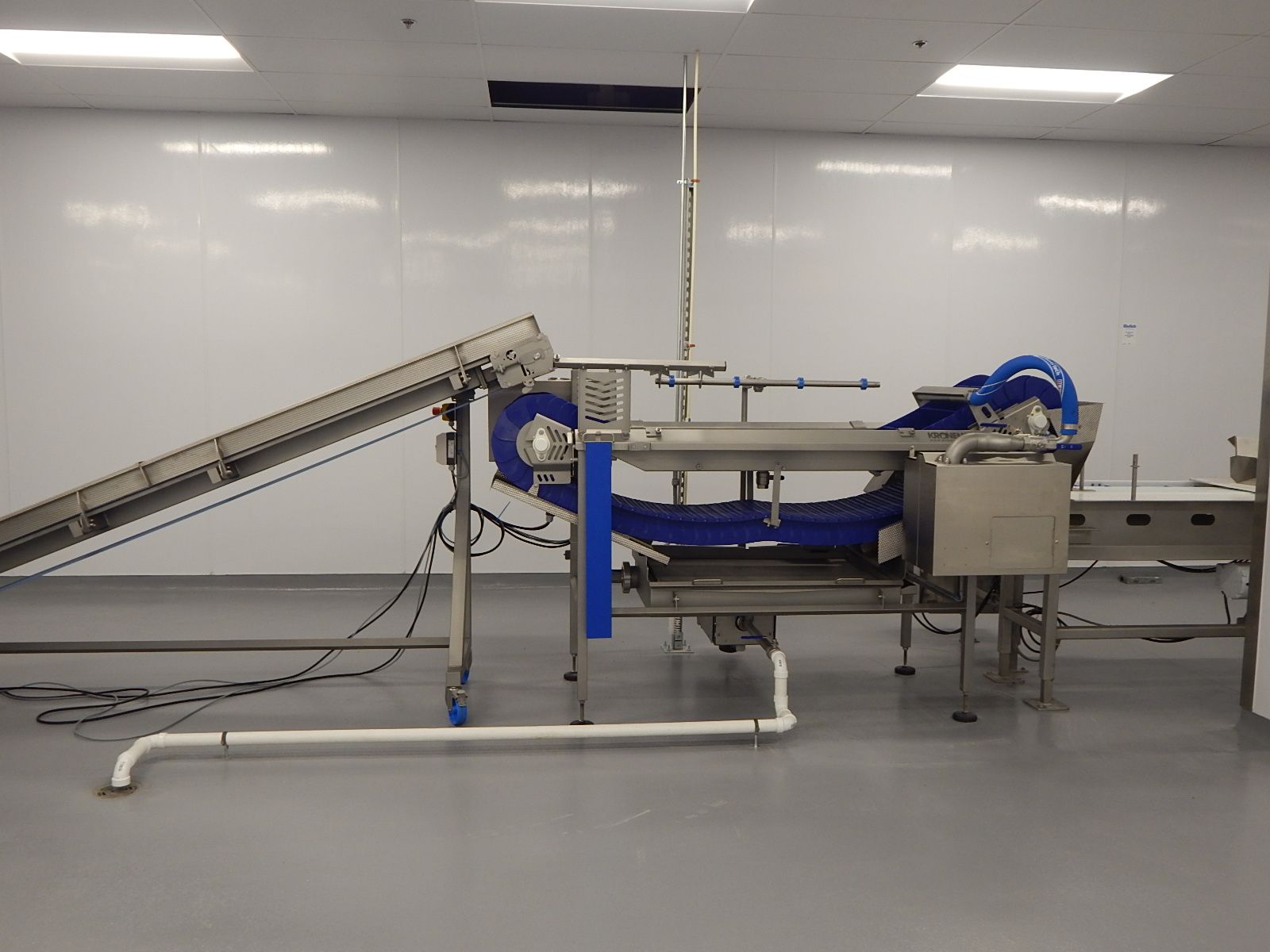 A stainless steel industrial food processing conveyor system with blue belts set in a white, sterile room.