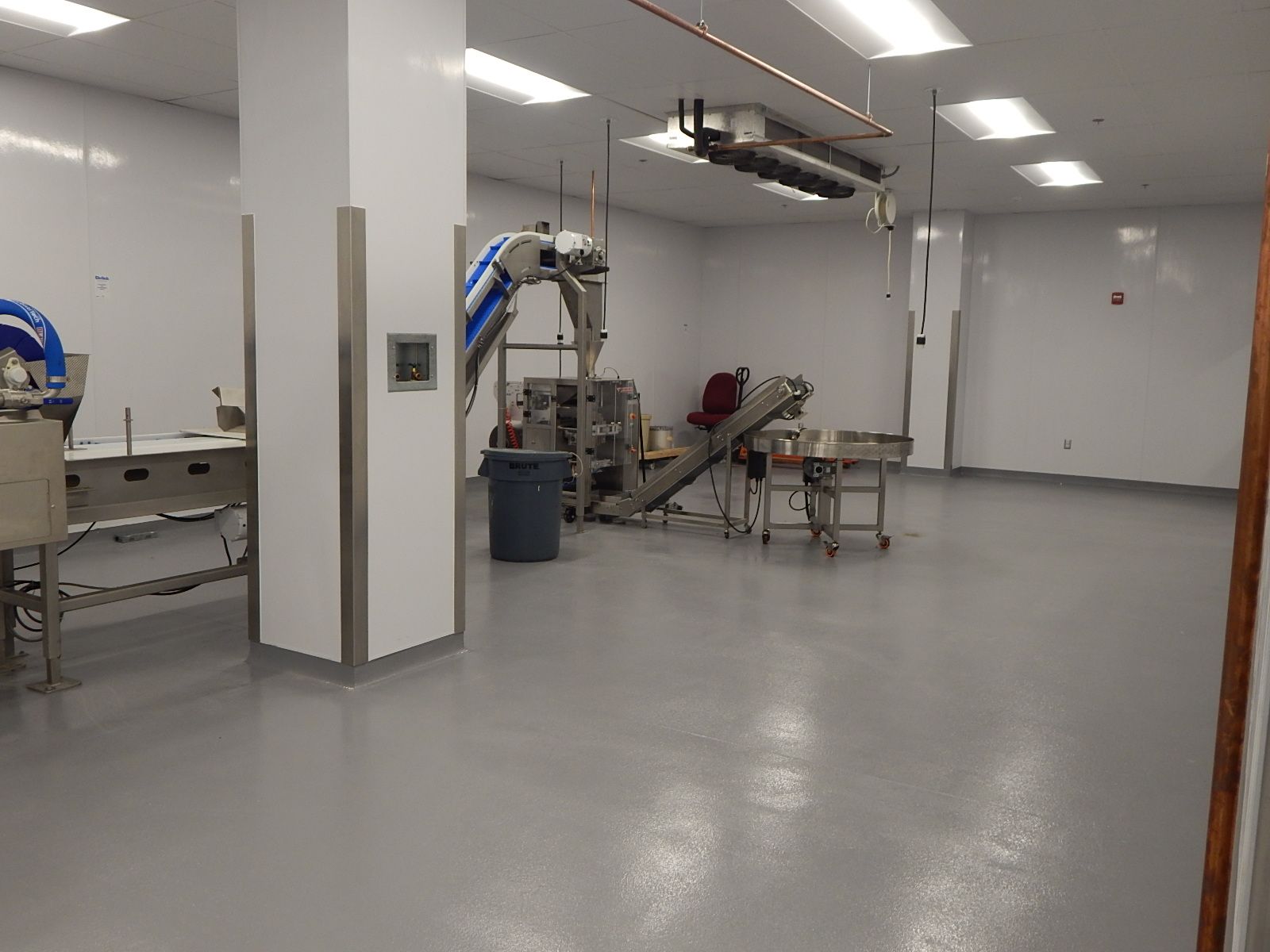 A clean, sterile industrial room with white walls, a gray floor, stainless steel equipment, and overhead lighting.