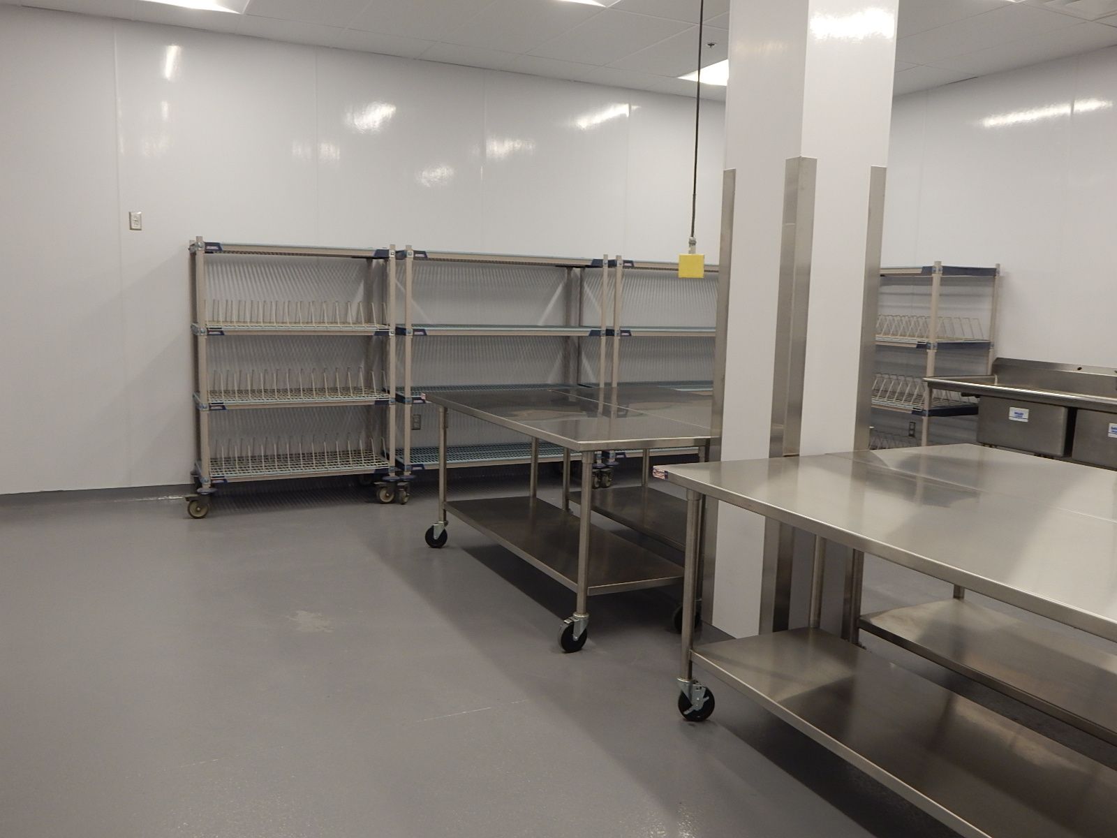 Stainless steel carts and work tables in a sterile, white, industrial or laboratory clean room with gray flooring.