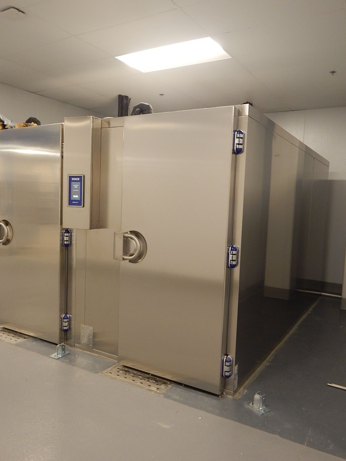 Large, stainless-steel industrial walk-in freezer units with digital control panels, set in a clean, commercial facility.
