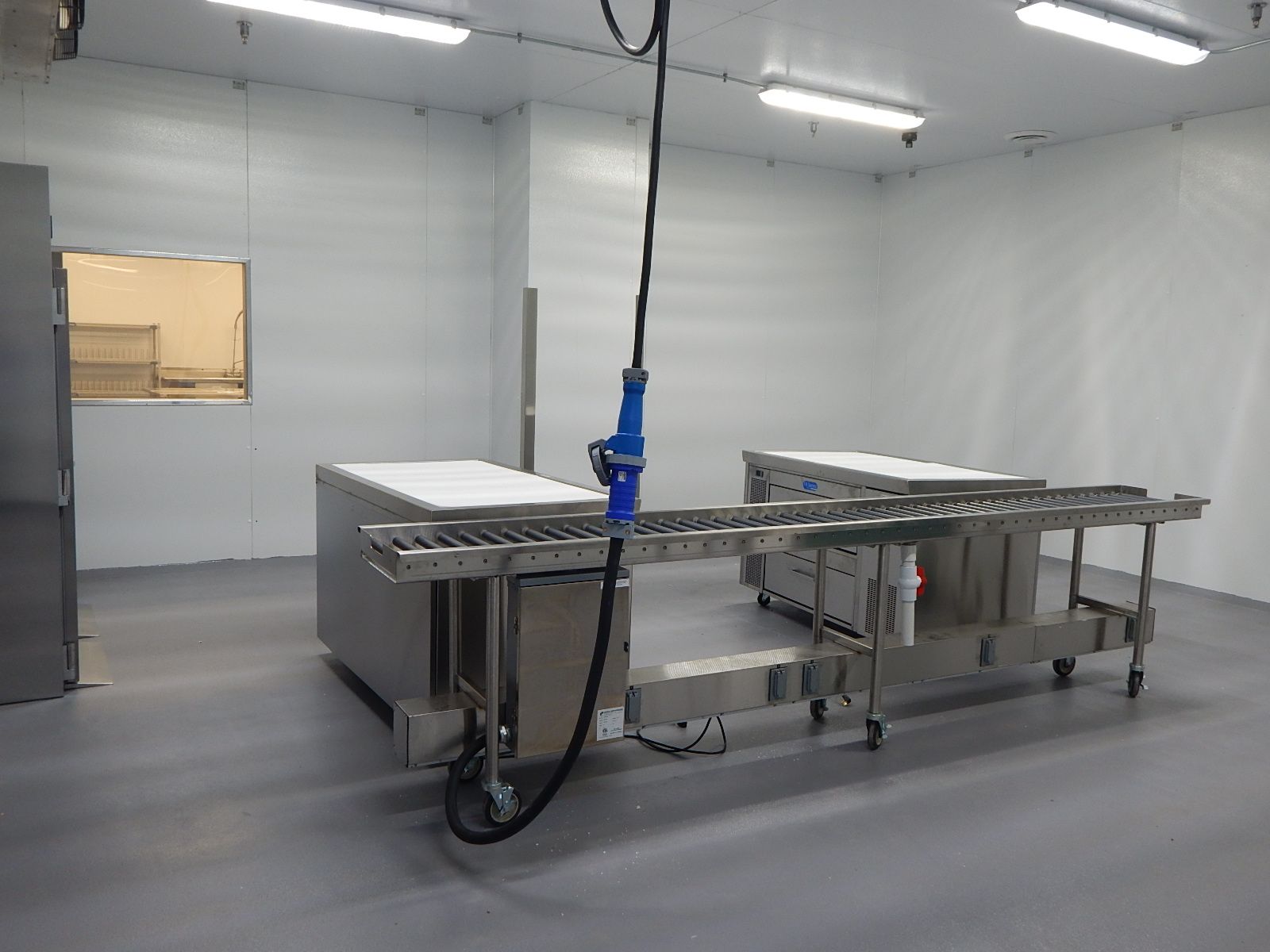 Industrial clean room featuring stainless steel workstations and a conveyor belt system with an overhead power cable.
