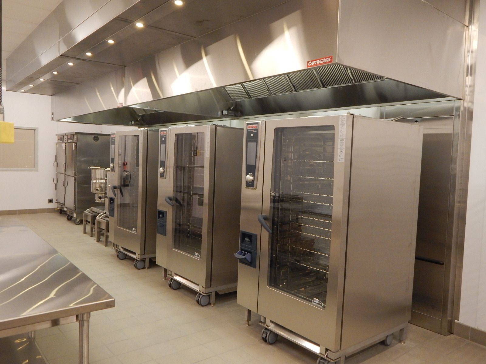 A commercial kitchen features a row of stainless steel Rational combi ovens under a large exhaust hood.
