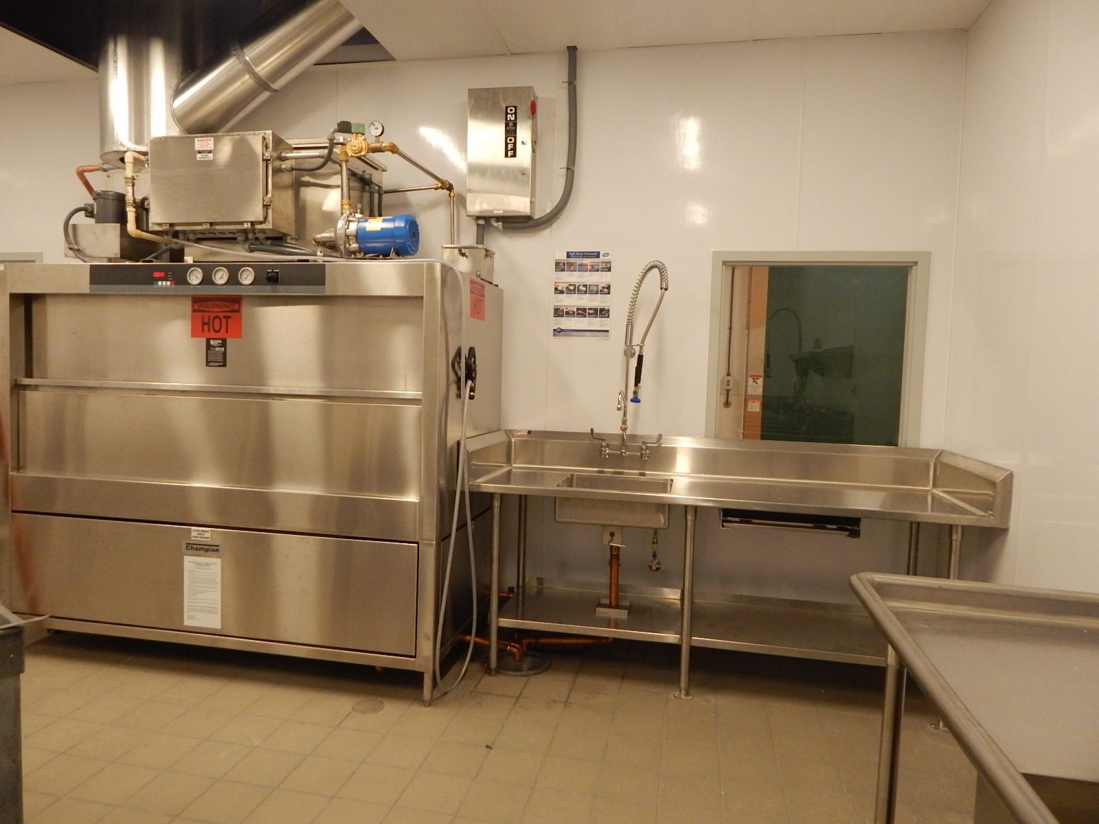 Industrial kitchen dishwashing station with a large stainless steel commercial dishwasher and adjacent sink.