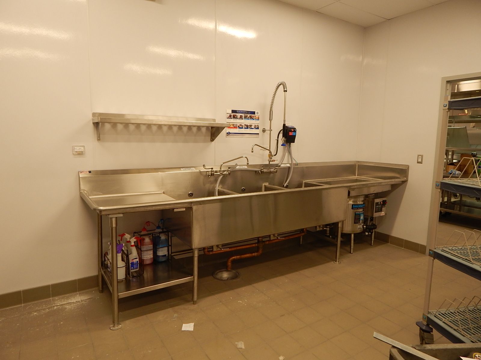 A commercial stainless steel three-compartment sink with a spray faucet in a clean kitchen room.