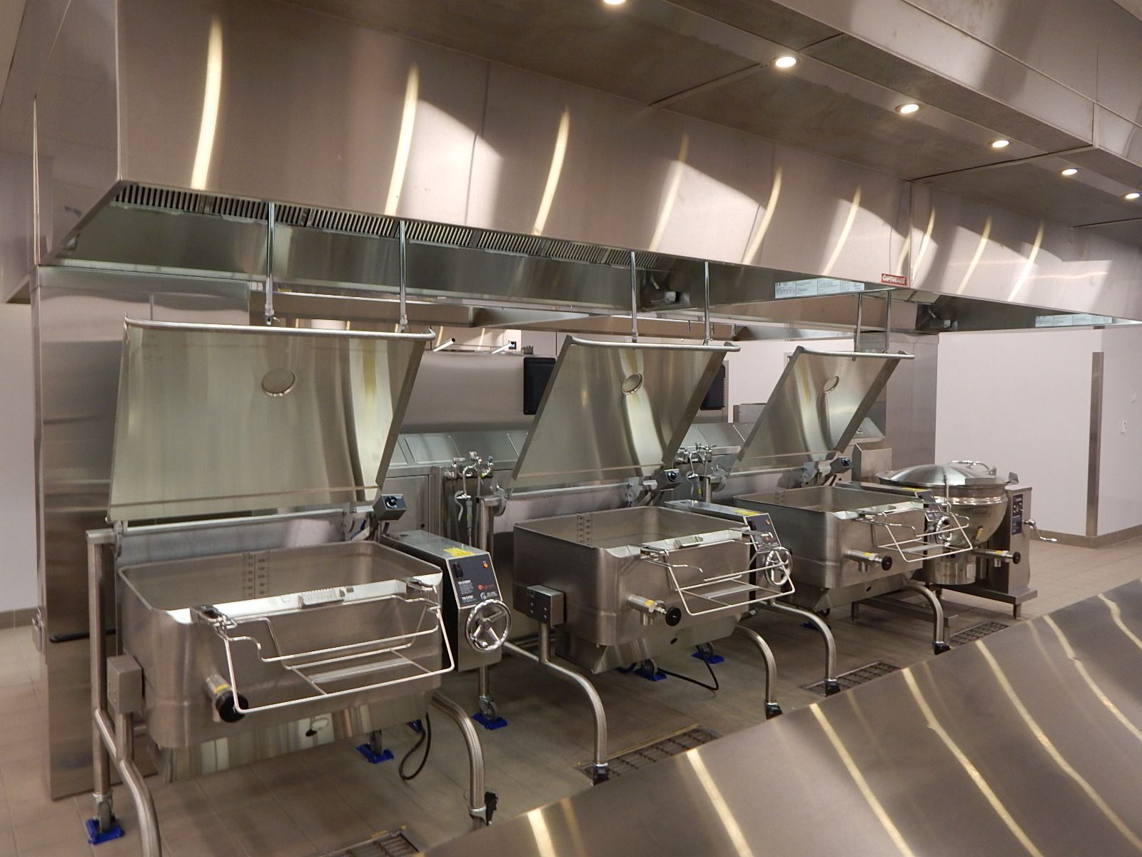 A row of stainless steel tilting braising pans with lids open in a professional commercial kitchen.