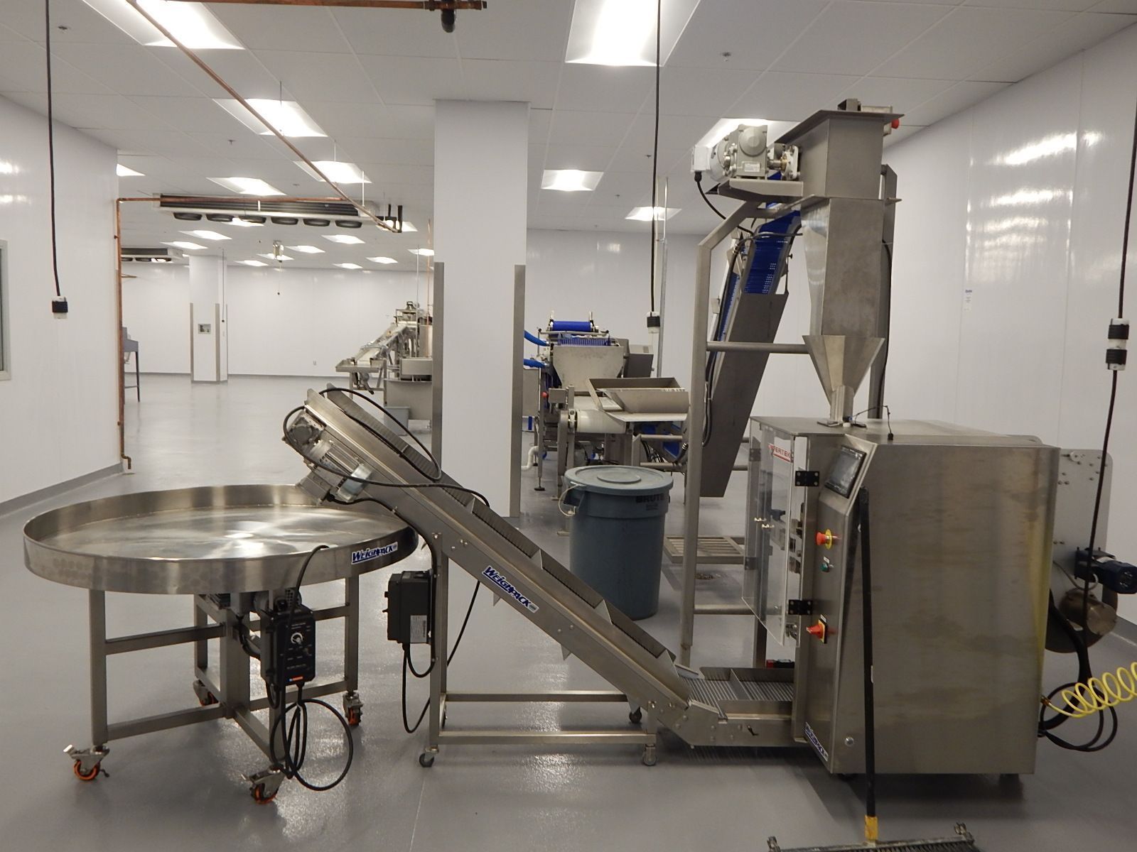 Stainless steel industrial packaging machinery in a bright, clean, sterile white facility.