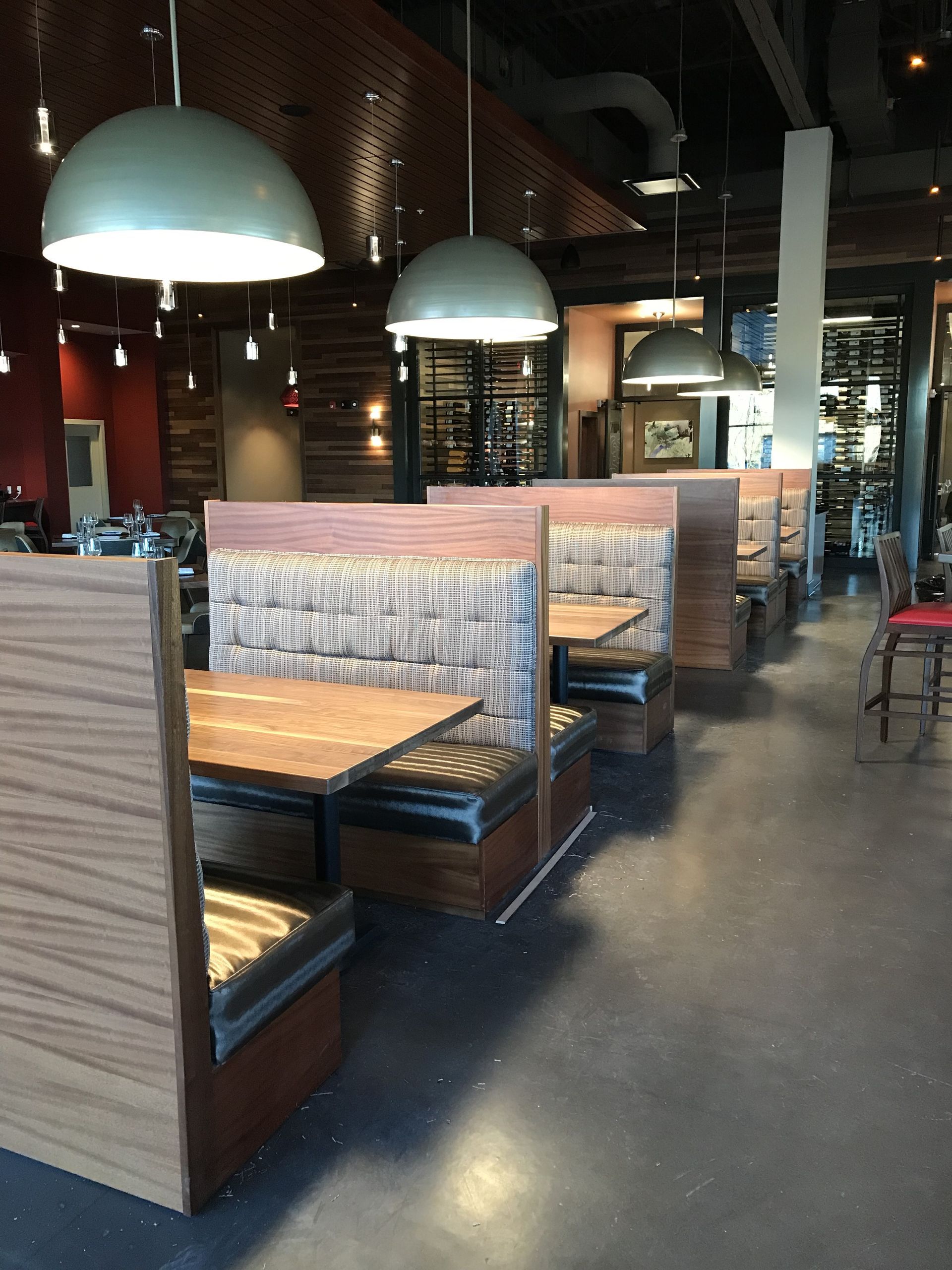 Empty restaurant interior featuring a row of wooden booths with patterned upholstery under large dome pendant lights.