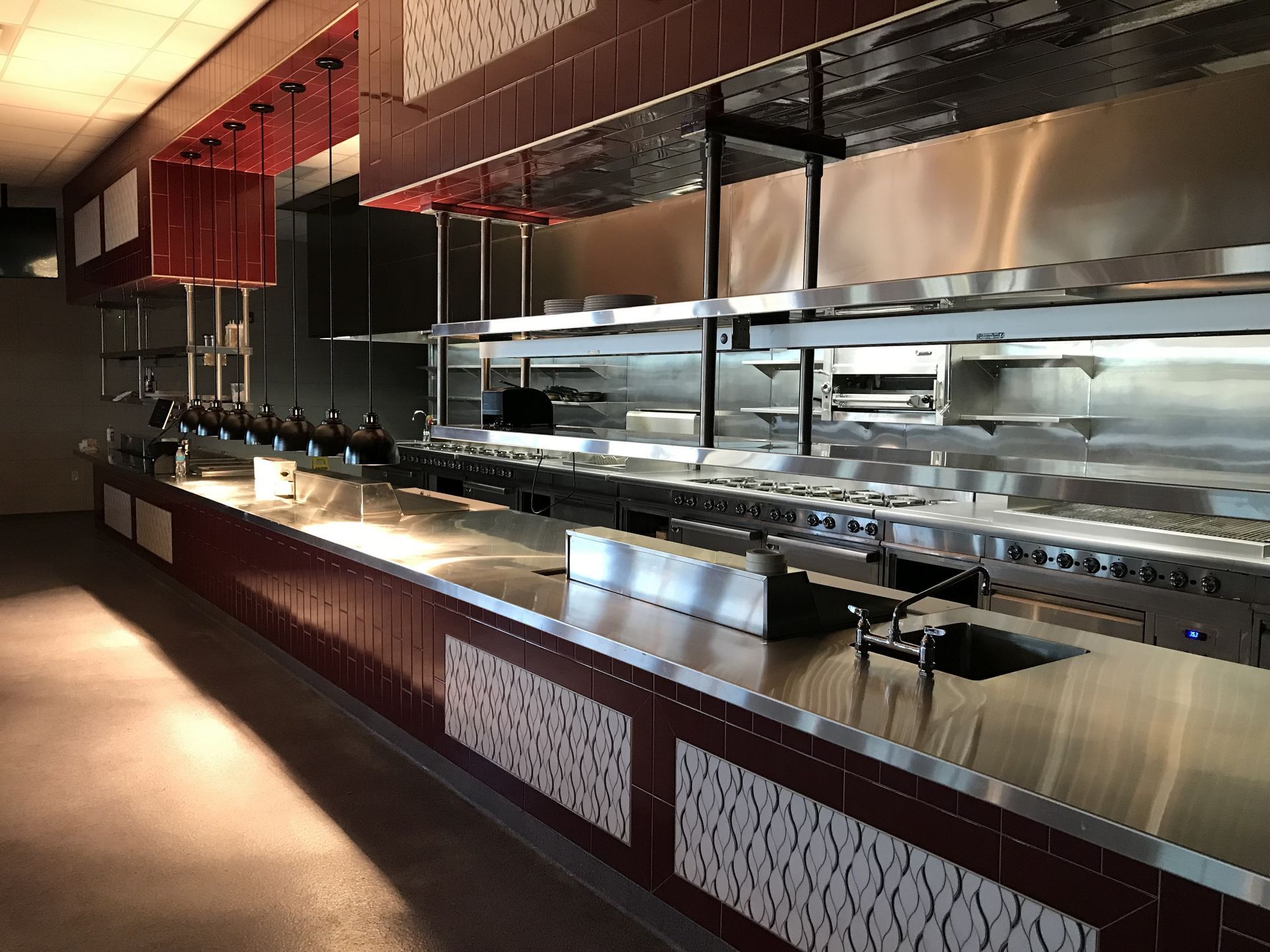 A modern, stainless steel commercial kitchen with a long counter and patterned decorative panels under the serving area.