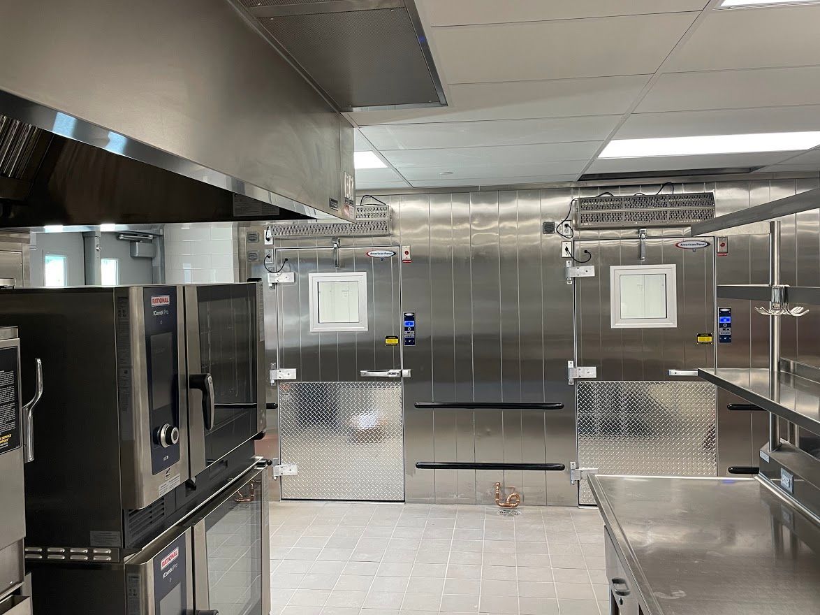 A commercial kitchen featuring stainless steel surfaces, a heavy-duty oven, and two walk-in refrigeration units.