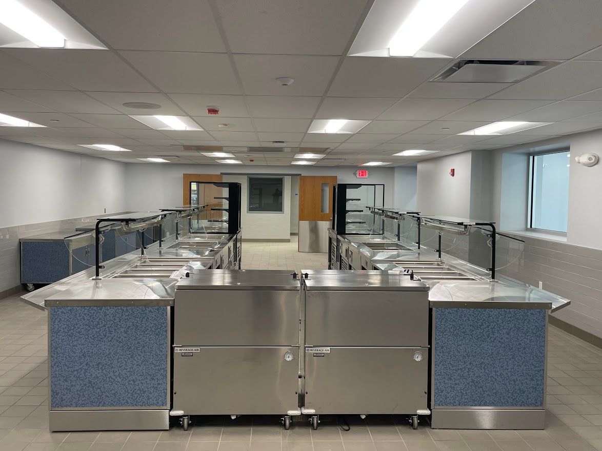 A commercial cafeteria serving line with stainless steel equipment and blue tiled accents in a well-lit room.