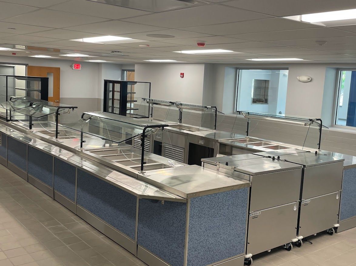 A food service buffet line with stainless steel equipment and blue textured bases in a brightly lit, empty room.